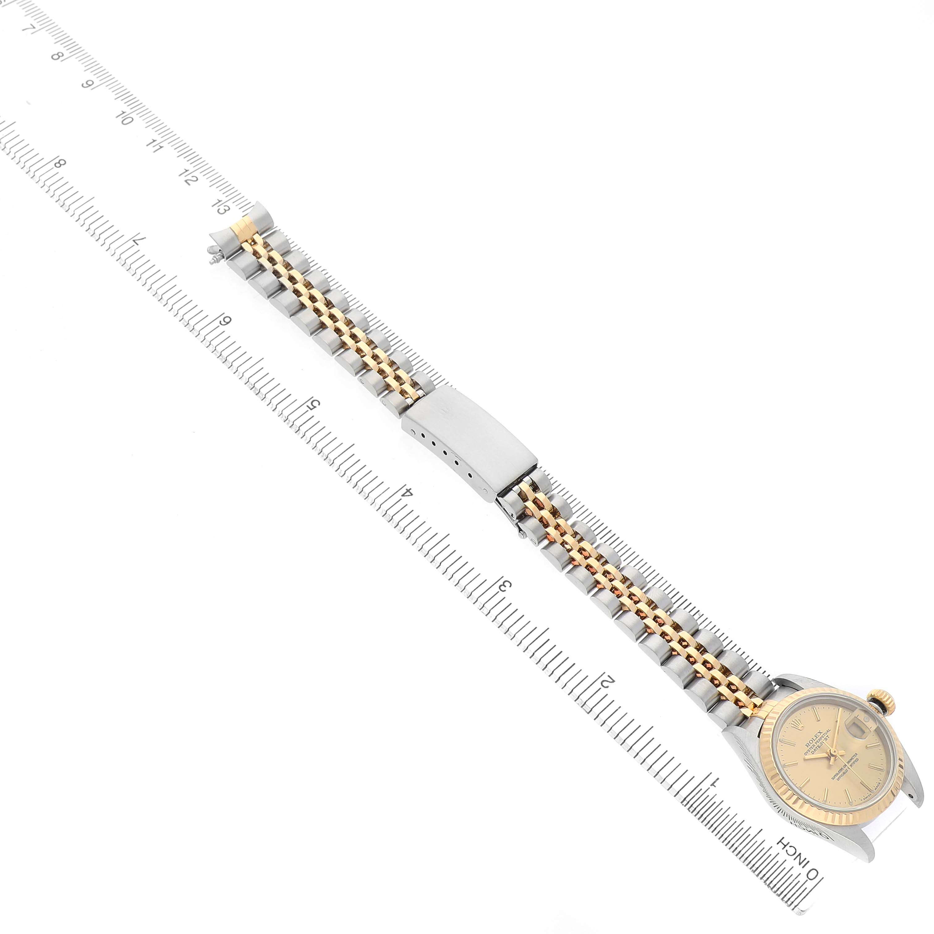 The image shows the Rolex Datejust 79173 Women's Steel and Gold (two tone) Champagne Dial watch at an angle highlighting its dial, jubilee bracelet, and clasp, alongside a ruler.