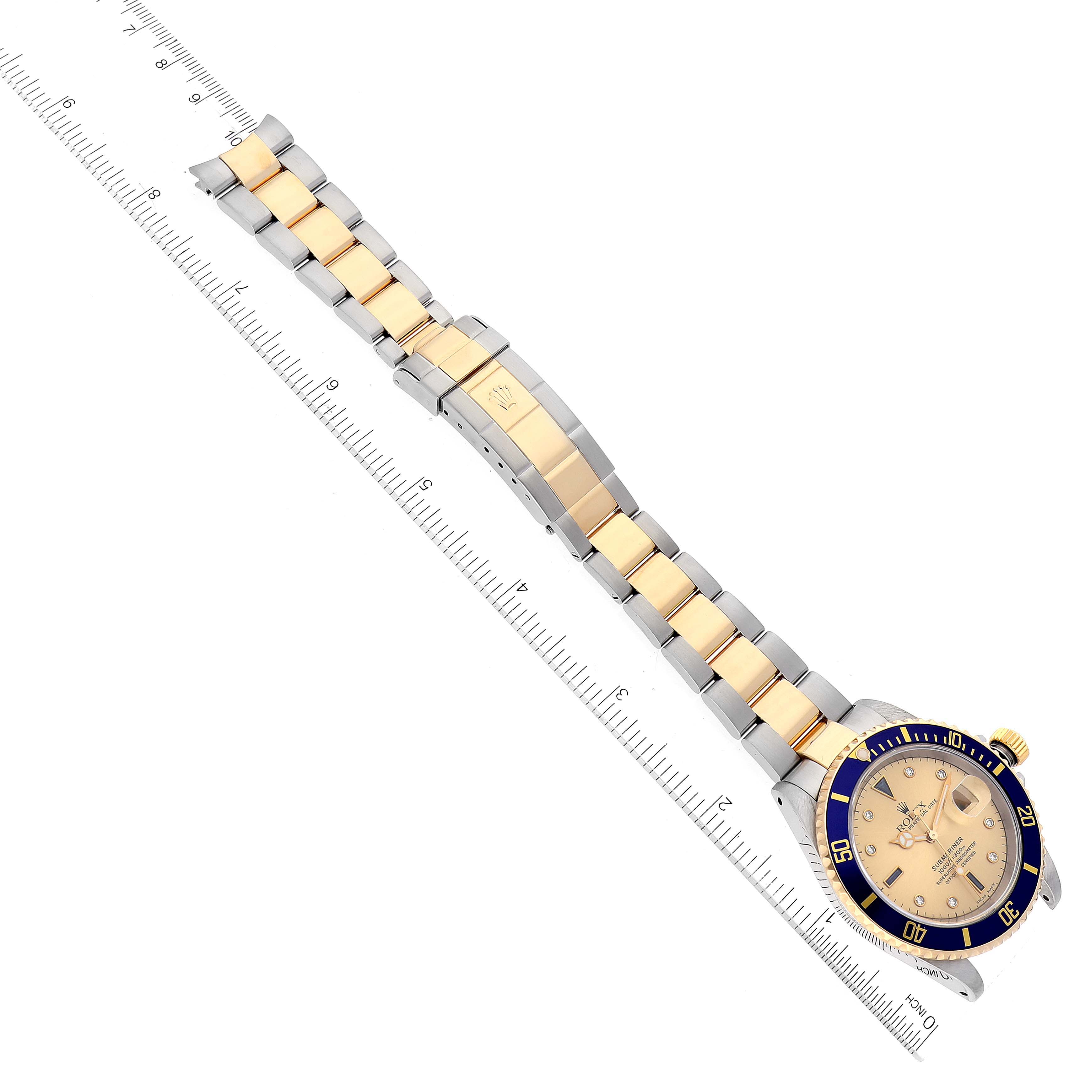 The image shows a full top view of a Rolex Submariner 16613 Men's Steel and Gold (two tone) Champagne Dial 16613 Men's Steel and Gold (two tone) Champagne Dial watch with its bracelet and clasp extended and aligned with a ruler.