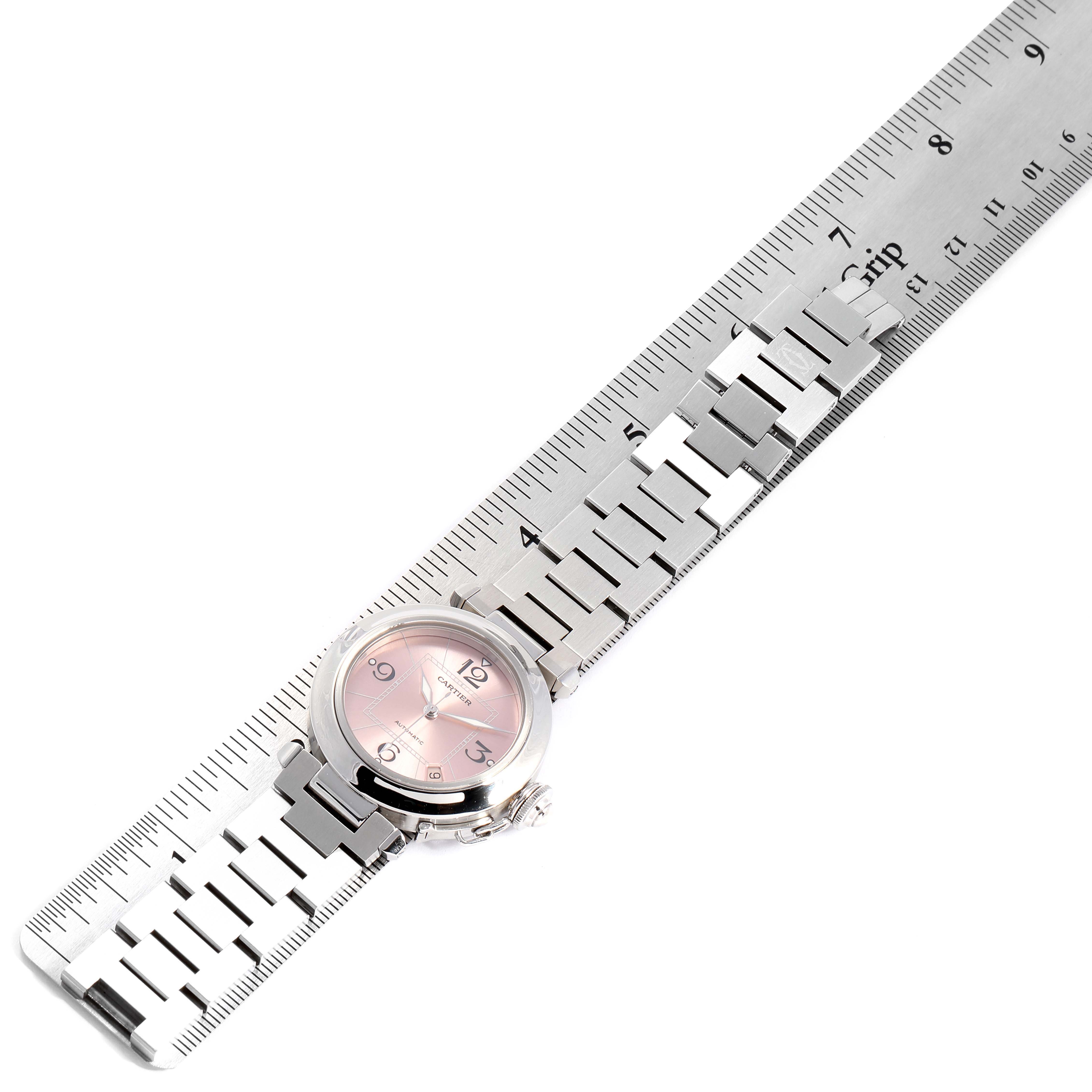 The Cartier Pasha W31075M7 Women's Stainless Steel Pink Dial W31075M7 Women's Stainless Steel Pink Dial watch is shown from a top-down angle with its metal bracelet laying alongside a ruler for scale.