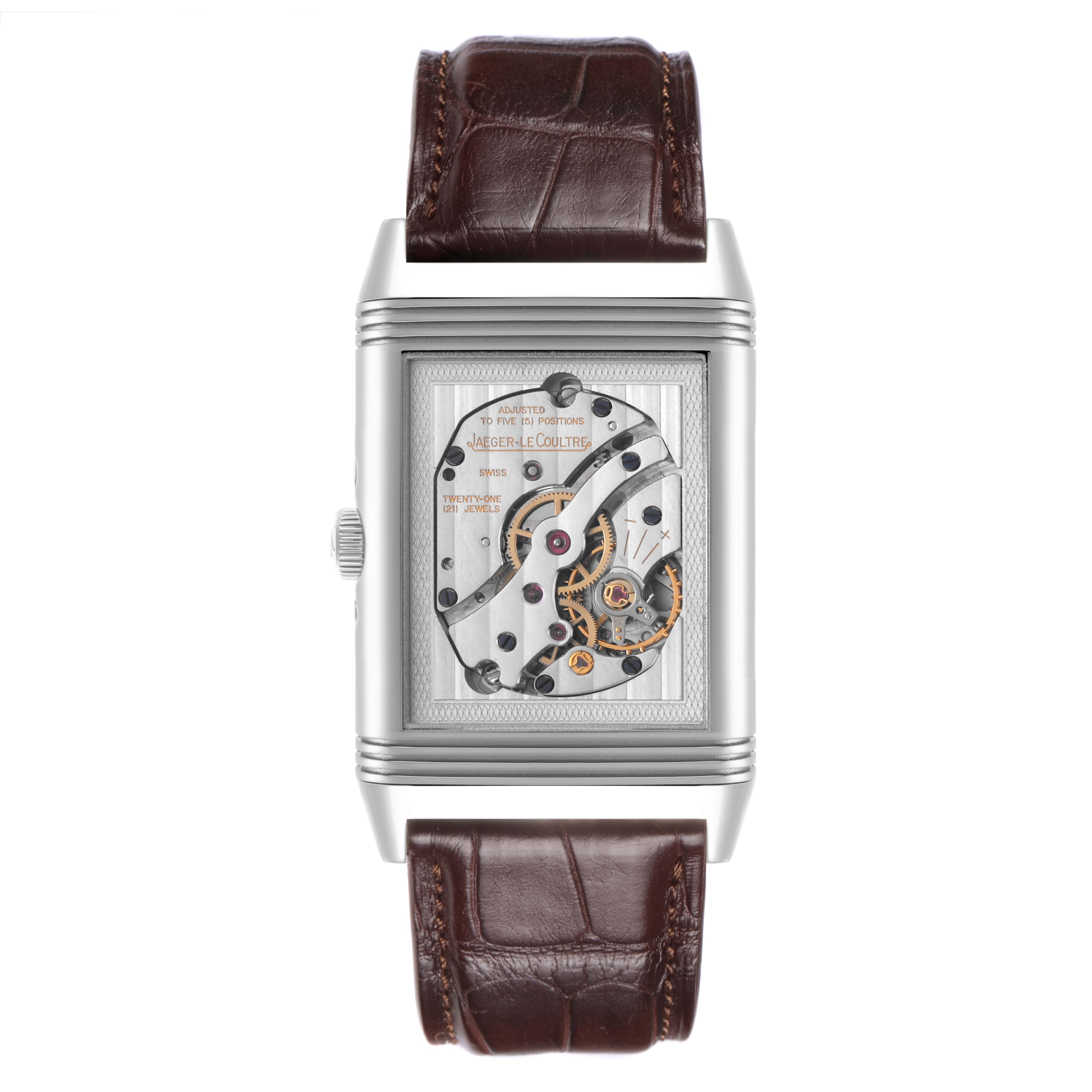 The Jaeger-LeCoultre Reverso watch is shown from the front, revealing the mechanical movement behind the reversible case.