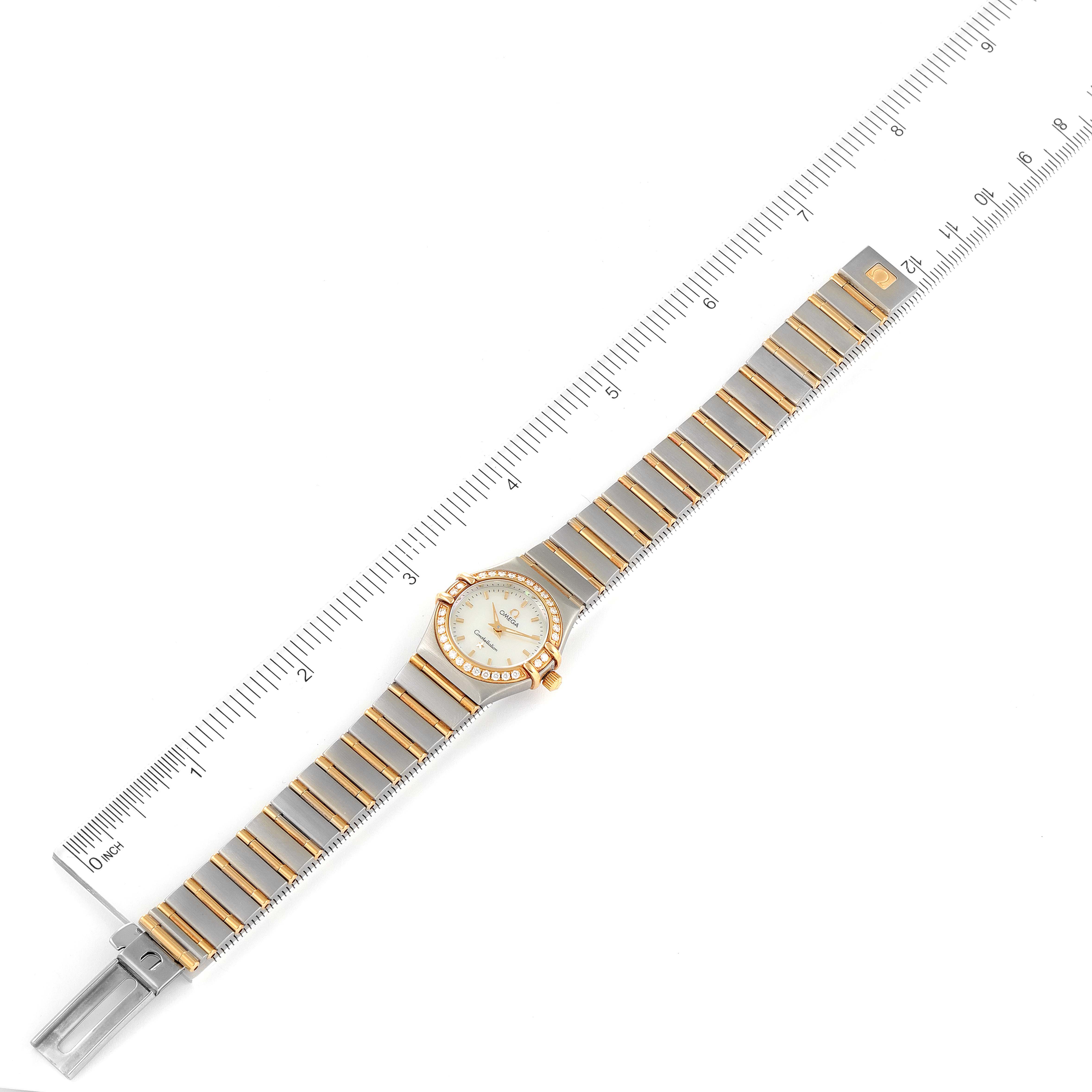 The Omega 1267.70.00 Women
s Steel and Gold (two tone) Mother of Pearl Dial 1267.70.00 Women
s Steel and Gold (two tone) Mother of Pearl Dial Constellation Steel Yellow Gold MOP Diamond Watch 1267.70.00 is shown from a top-down angle with a measuring scale beside it.