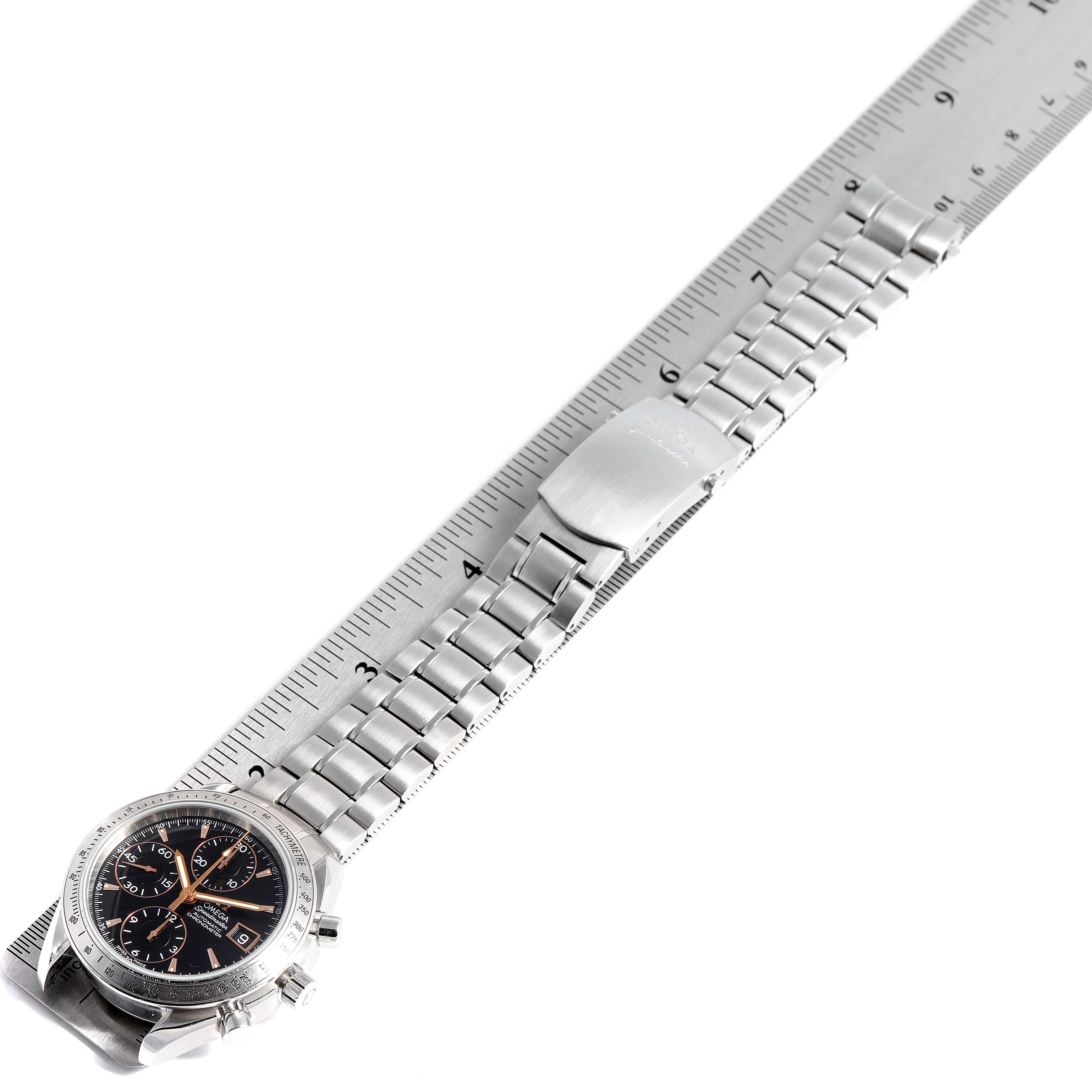 The image shows an Omega Speedmaster 3211.50.00 Men's Stainless Steel Black Dial 3211.50.00 Men's Stainless Steel Black Dial watch laid flat on a ruler, displaying its stainless steel bracelet and clasp.