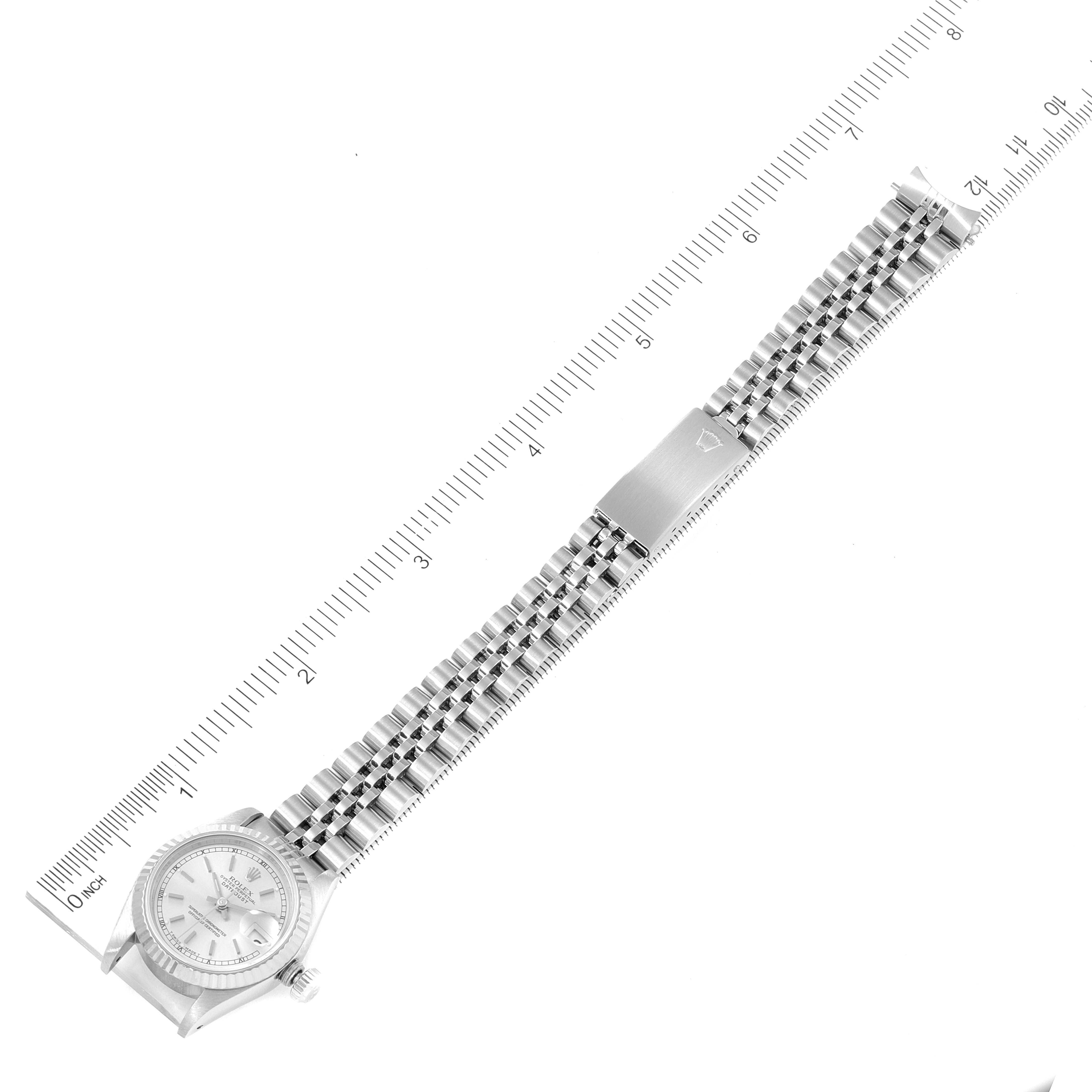 The Rolex Datejust 69174 Women
s Stainless Steel Silver Dial 69174 Women
s Stainless Steel Silver Dial watch is shown laid flat, displaying the entire face, bracelet, and clasp, alongside a ruler for scale.