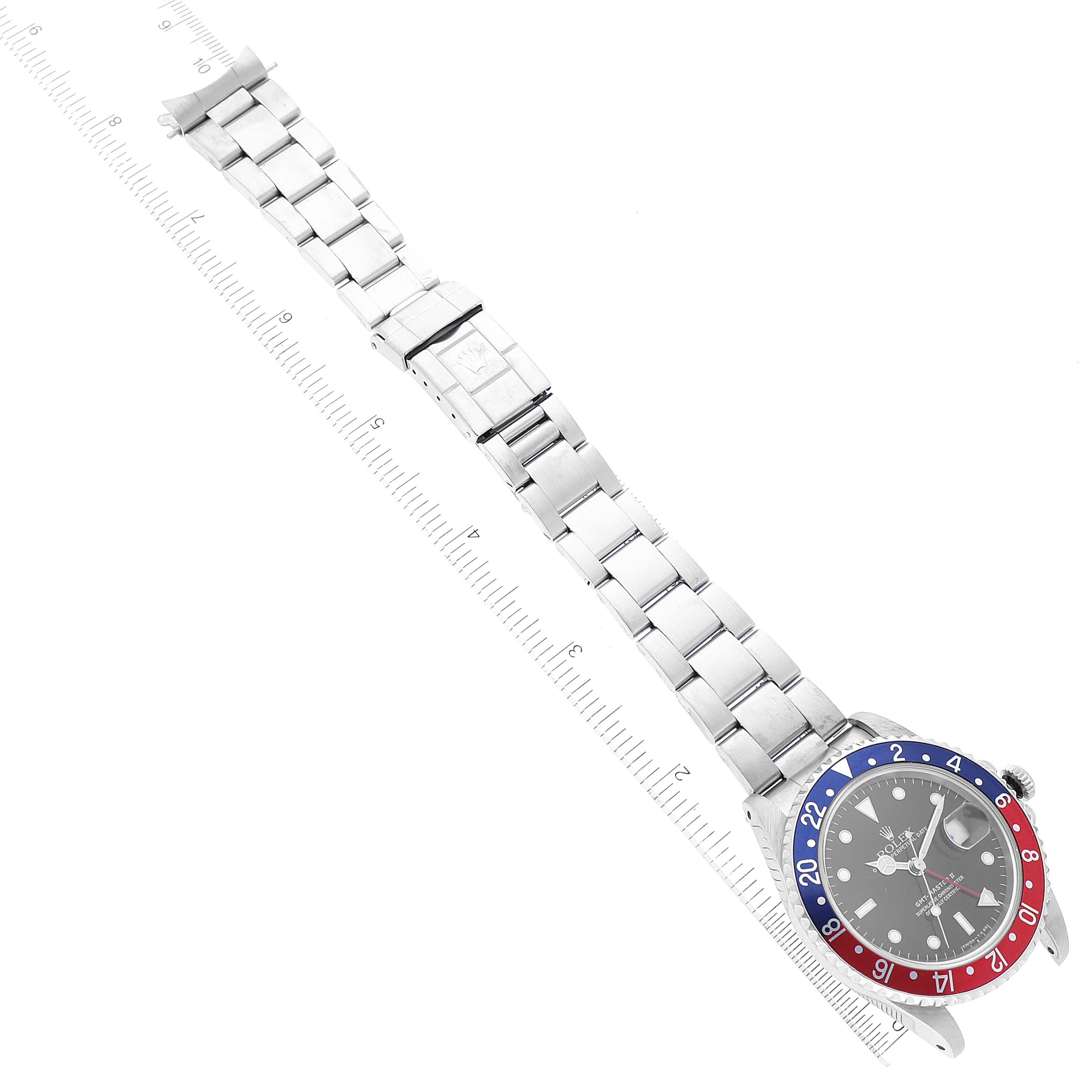 This image shows a Rolex GMT-Master 16710 Men
s Stainless Steel Black Dial 16710 Men
s Stainless Steel Black Dial watch laid flat with its full bracelet and a ruler for measurement.