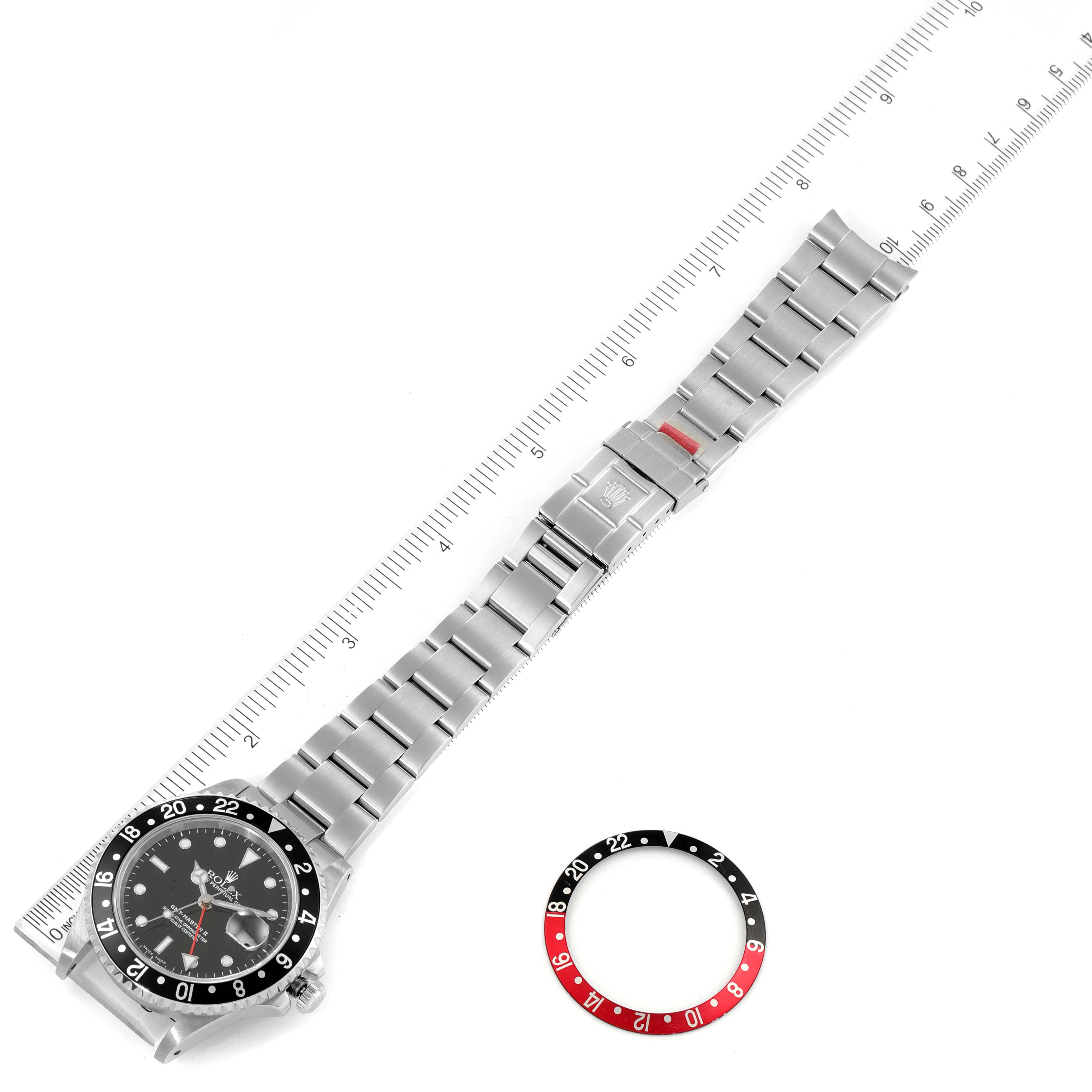 The Rolex GMT-Master 16710 Men
s Stainless Steel Black Dial 16710 Men
s Stainless Steel Black Dial watch is shown lying flat with a ruler for scale and an extra black-and-red bezel beside it.