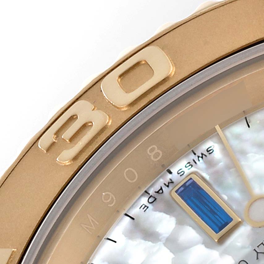 The image shows a close-up of the bezel and dial of a Rolex Yacht-Master 16628B Men's Yellow Gold Mother of Pearl Dial 16628B Men's Yellow Gold Mother of Pearl Dial watch, featuring gold markings and a blue gemstone.