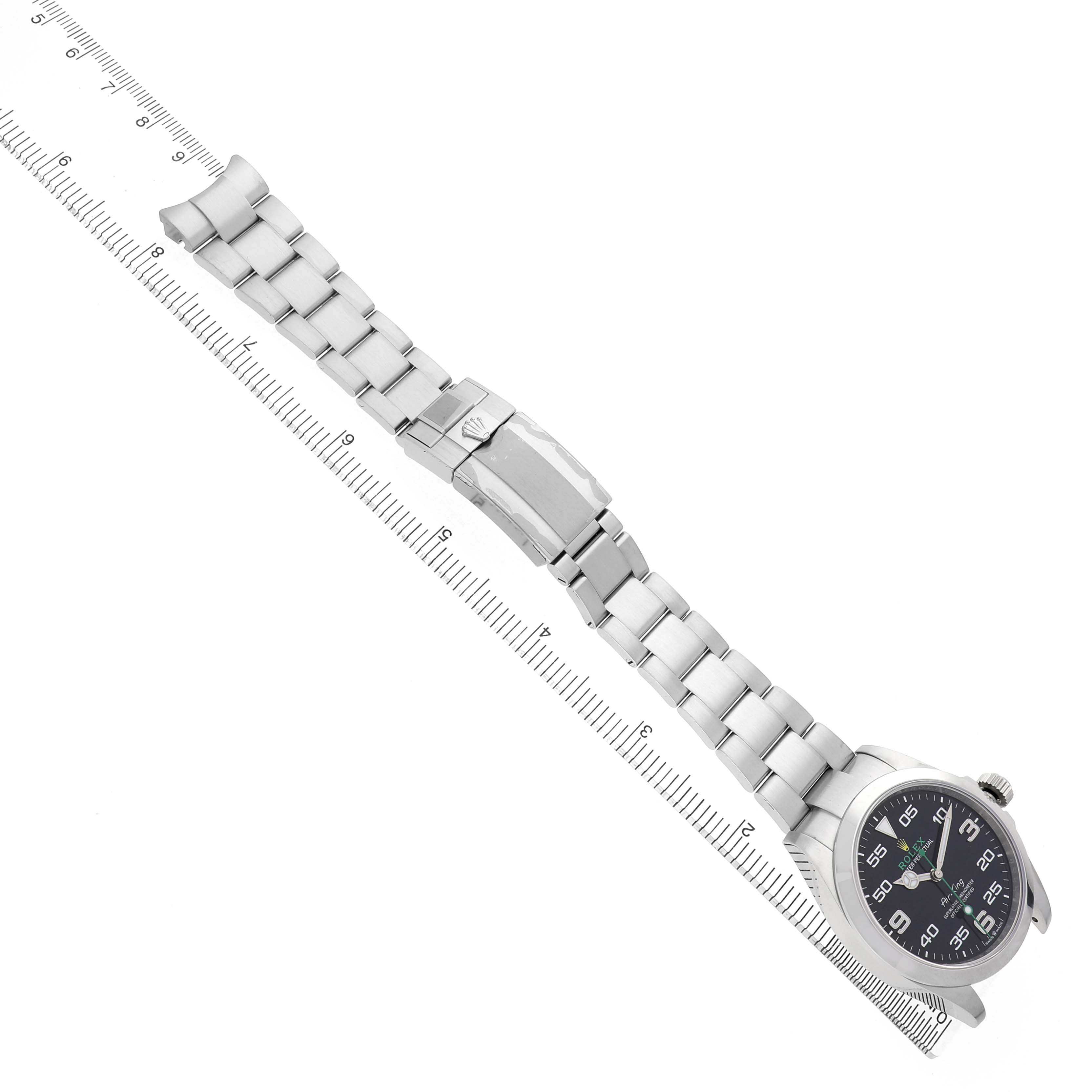 The Rolex Air-King 126900 Men's Stainless Steel Black Dial watch is shown from an overhead angle, displaying the full bracelet, clasp, and face with a ruler alongside.