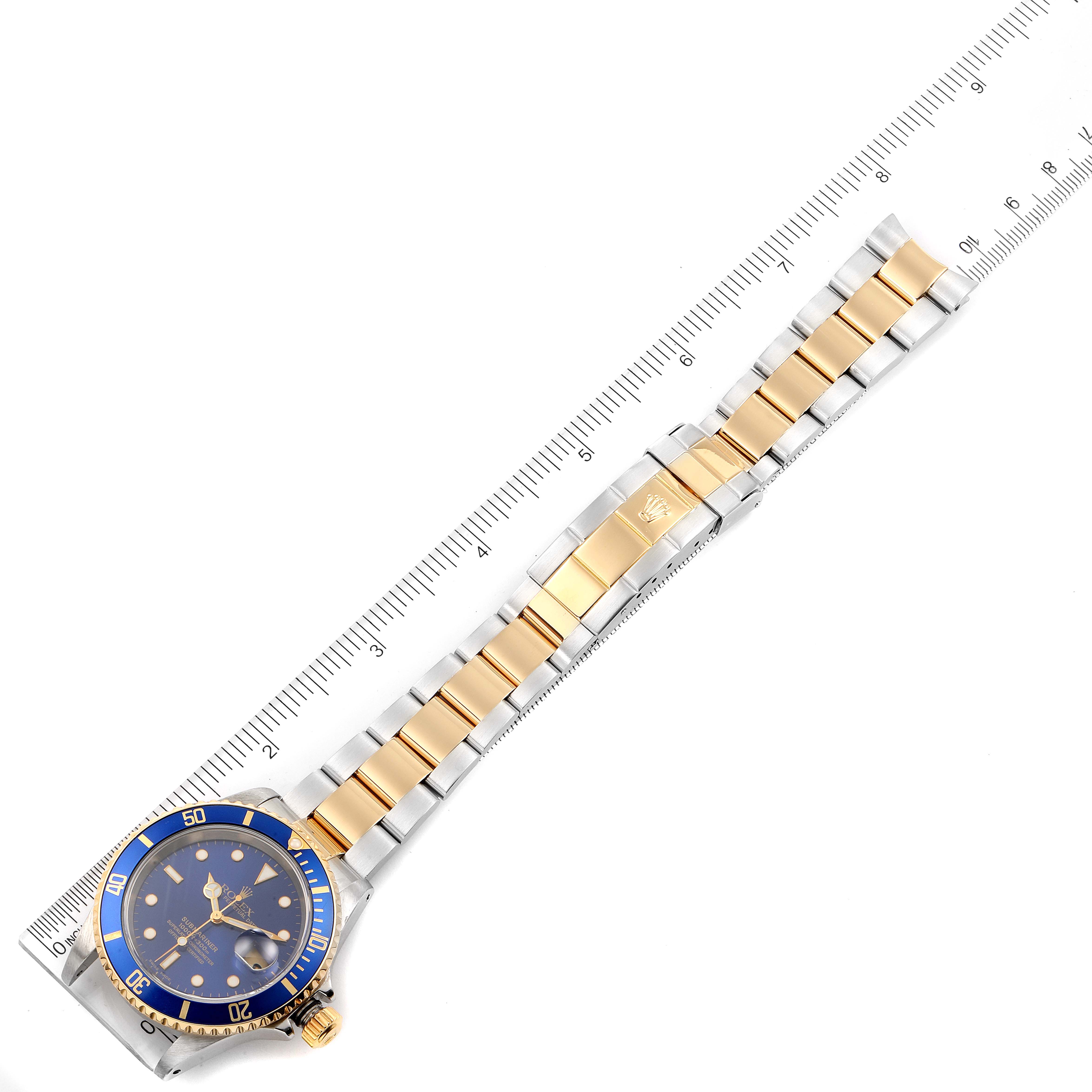 This image shows a top view of a Rolex Submariner 16613 Men's Steel and Gold (two tone) Blue Dial 16613 Men's Steel and Gold (two tone) Blue Dial watch with its full bracelet displayed against a ruler for scale.