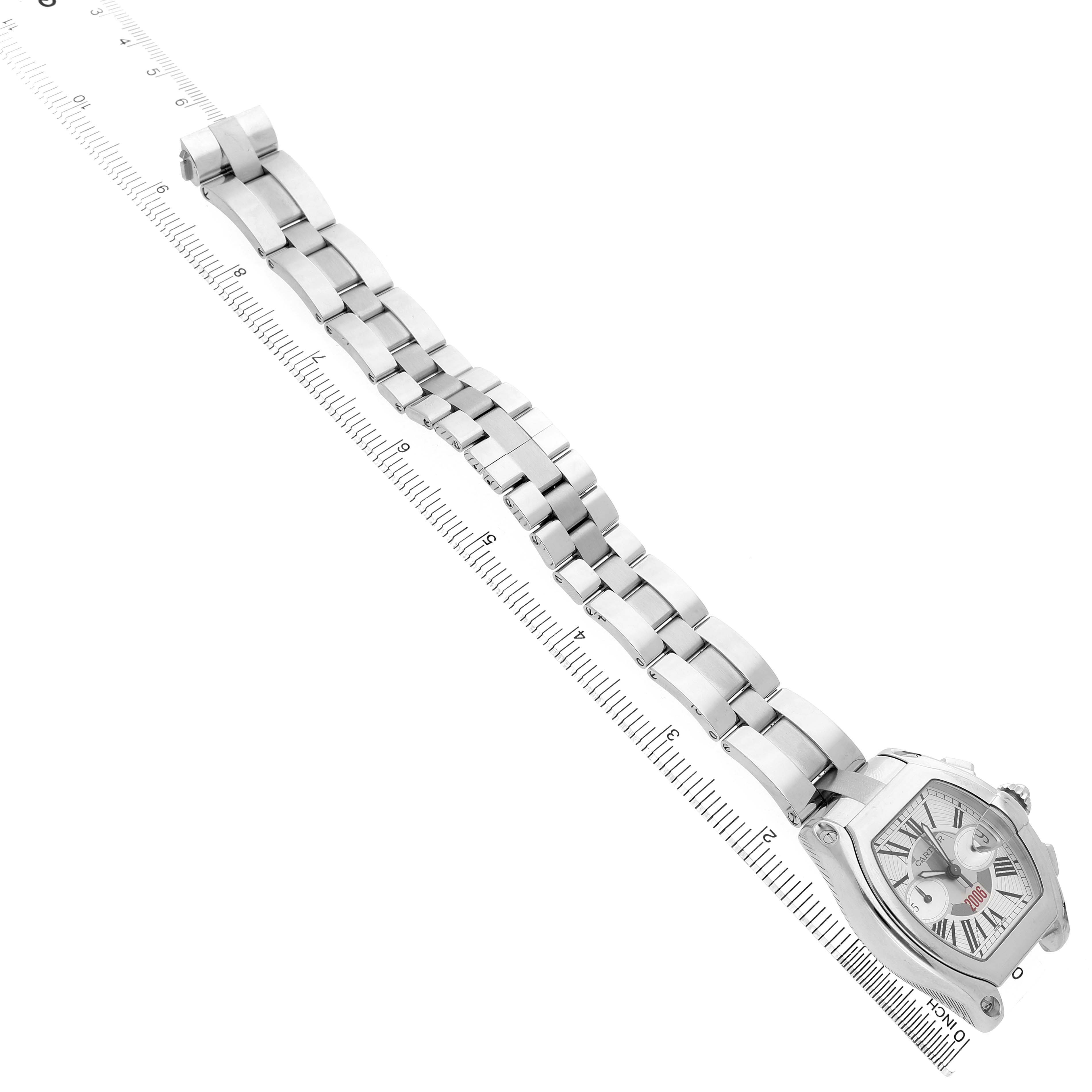 The image shows a Cartier Roadster W62044X6 Men's Stainless Steel Silver Dial watch angled diagonally with a focus on its face and metal bracelet, alongside a ruler.