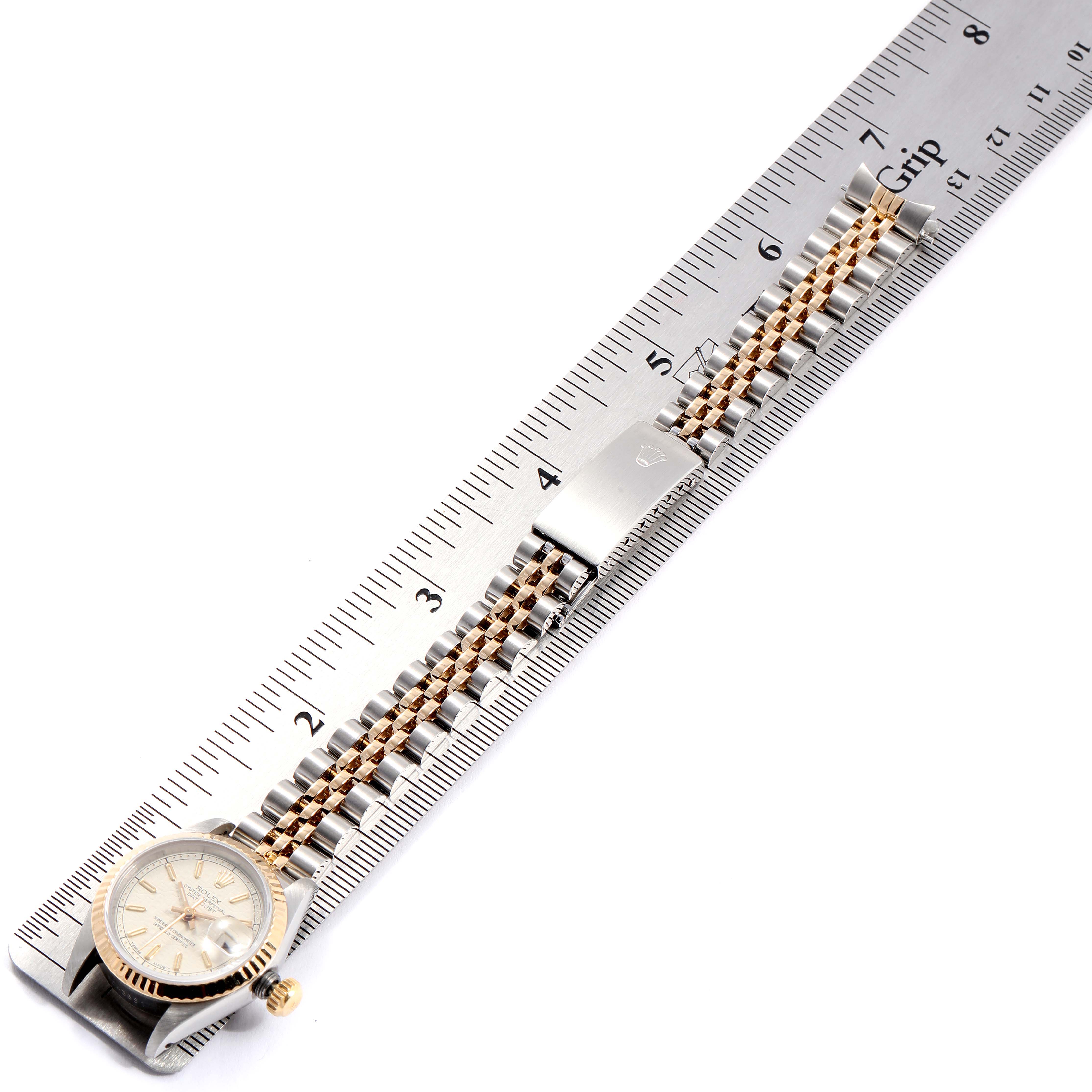 The Rolex 69173 Women's Stainless Steel Beige Dial 69173 Women's Stainless Steel Beige Dial Datejust Steel Yellow Gold Anniversary Dial Ladies Watch 69173 is shown laid flat next to a ruler, highlighting its length.