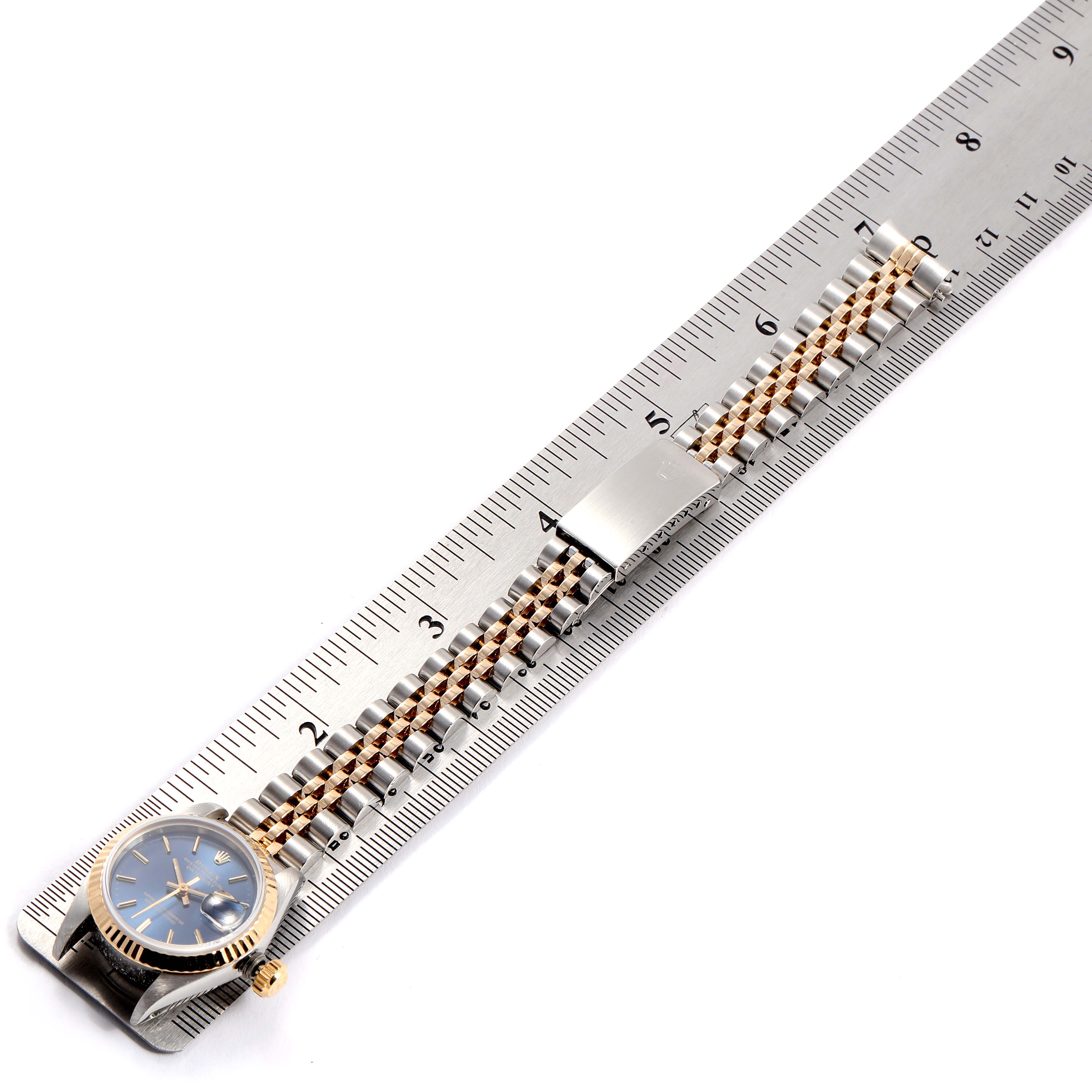 The Rolex Datejust 69173 Women
s Stainless Steel Blue Dial 69173 Women
s Stainless Steel Blue Dial watch is shown laid flat against a ruler, displaying its face, bracelet, and clasp.