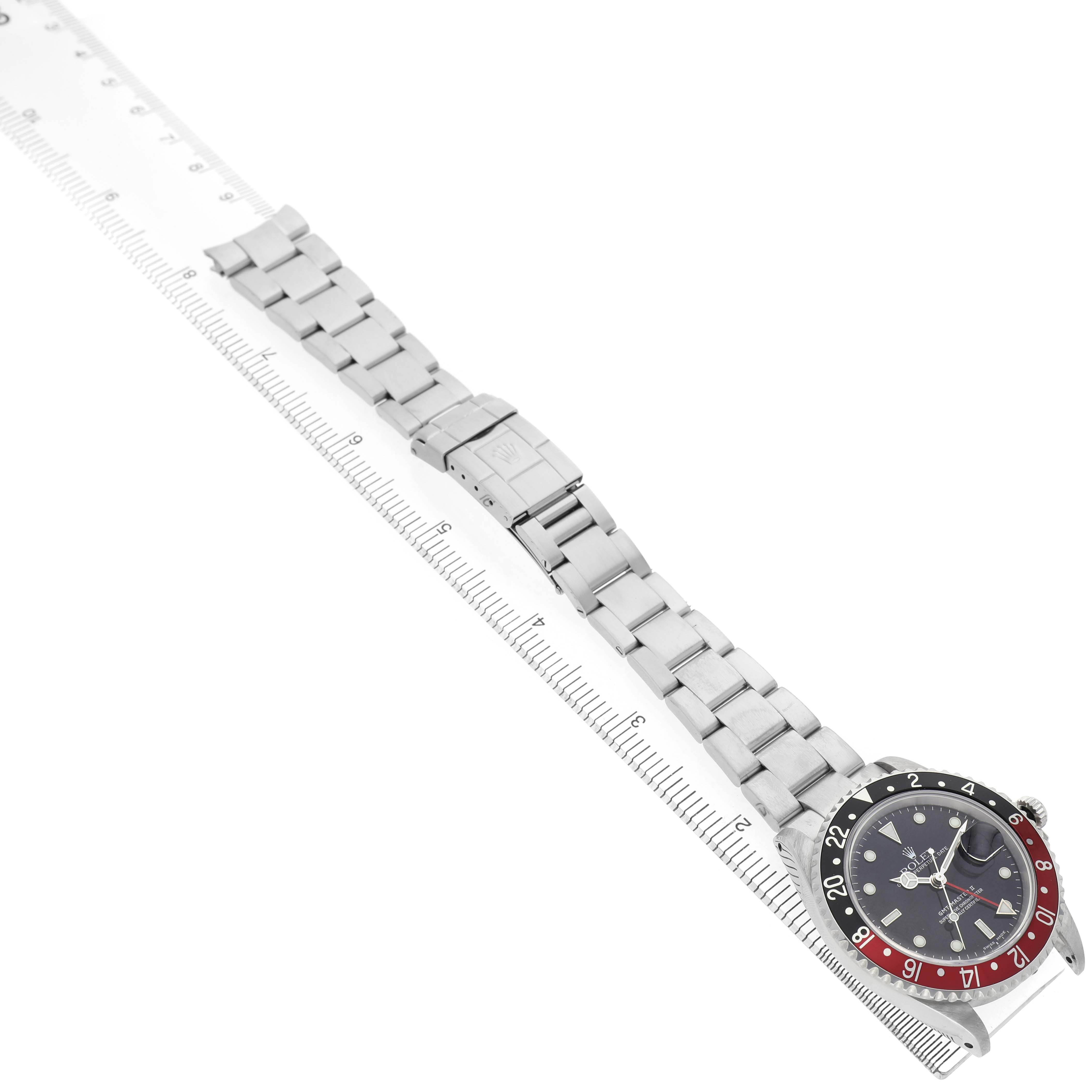 The Rolex GMT-Master 16710 Men's Stainless Steel Black Dial watch is shown from an overhead angle, displaying the bracelet, clasp, and watch face with a ruler for scale.