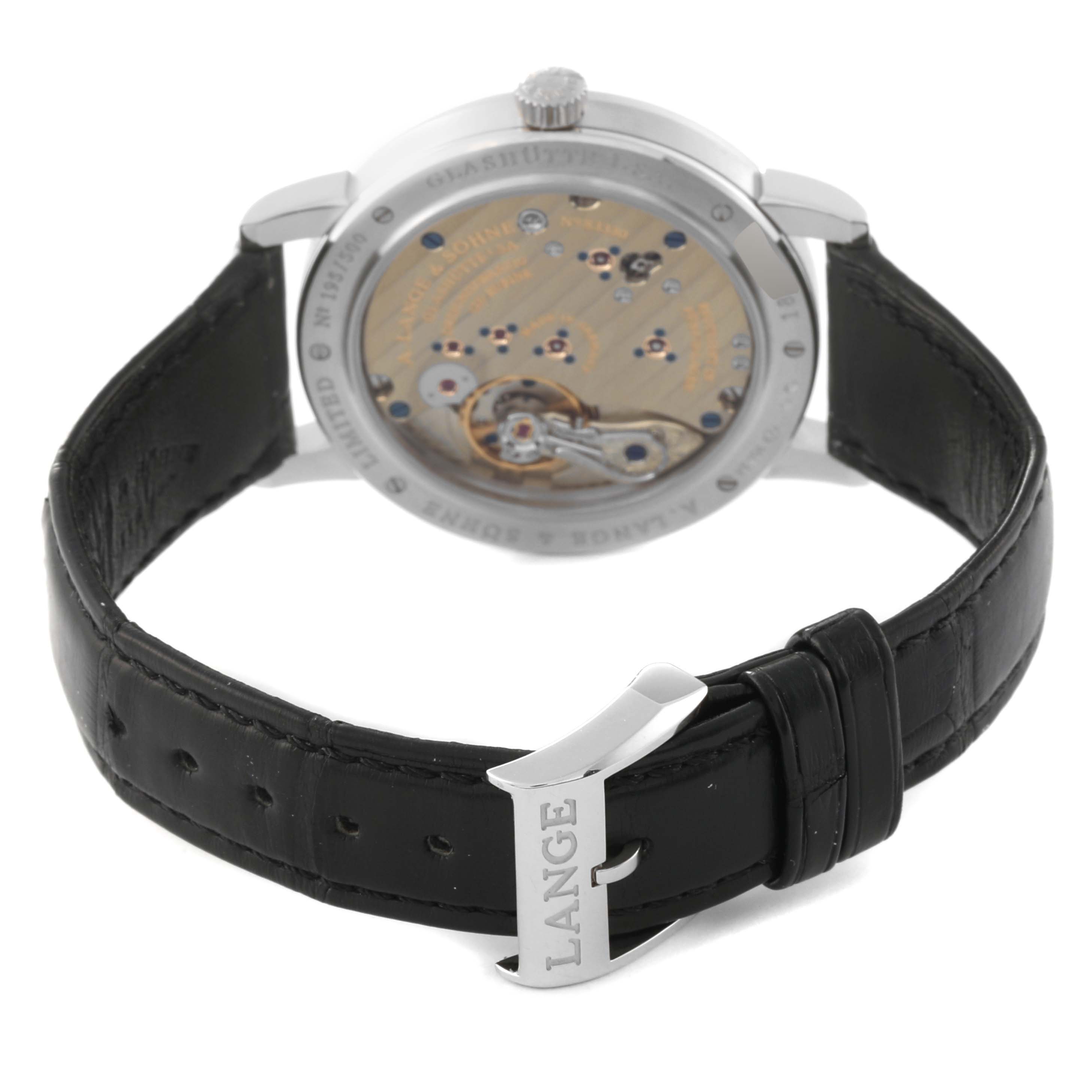 The image shows the back view of an A. Lange & Sohne 1815 233.025 Men's Platinum Silver Dial watch, focusing on its exposed movement and black leather strap with a "LANGE" buckle.