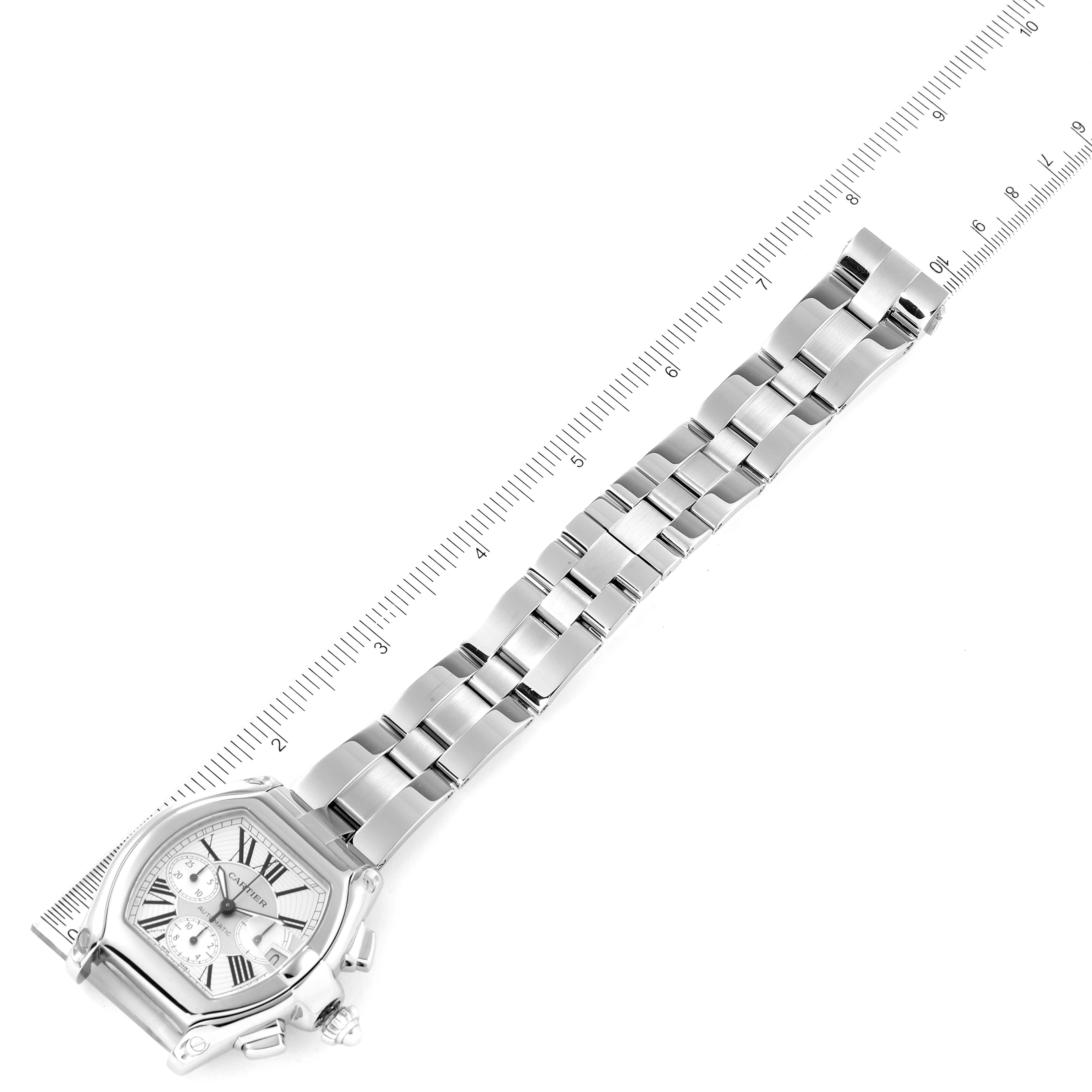 The image shows a Cartier Roadster W62019X6 Men
s Stainless Steel Silver Dial W62019X6 Men
s Stainless Steel Silver Dial watch placed diagonally next to a ruler, displaying the watch face and metal bracelet.