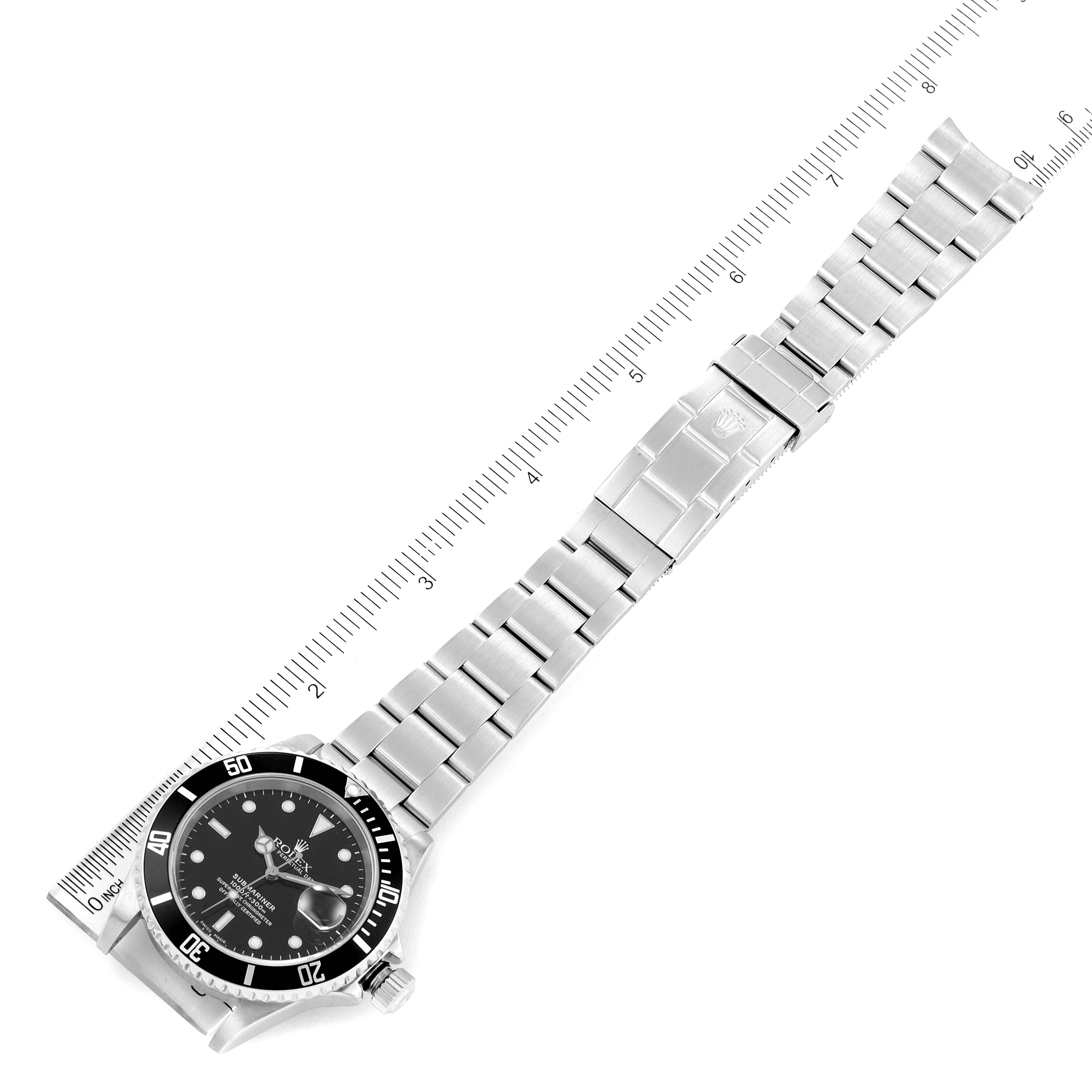 The image shows a top-down view of a Rolex Submariner 16610 Men
s Stainless Steel Black Dial 16610 Men
s Stainless Steel Black Dial watch including its face and stainless steel bracelet, alongside a ruler for scale.