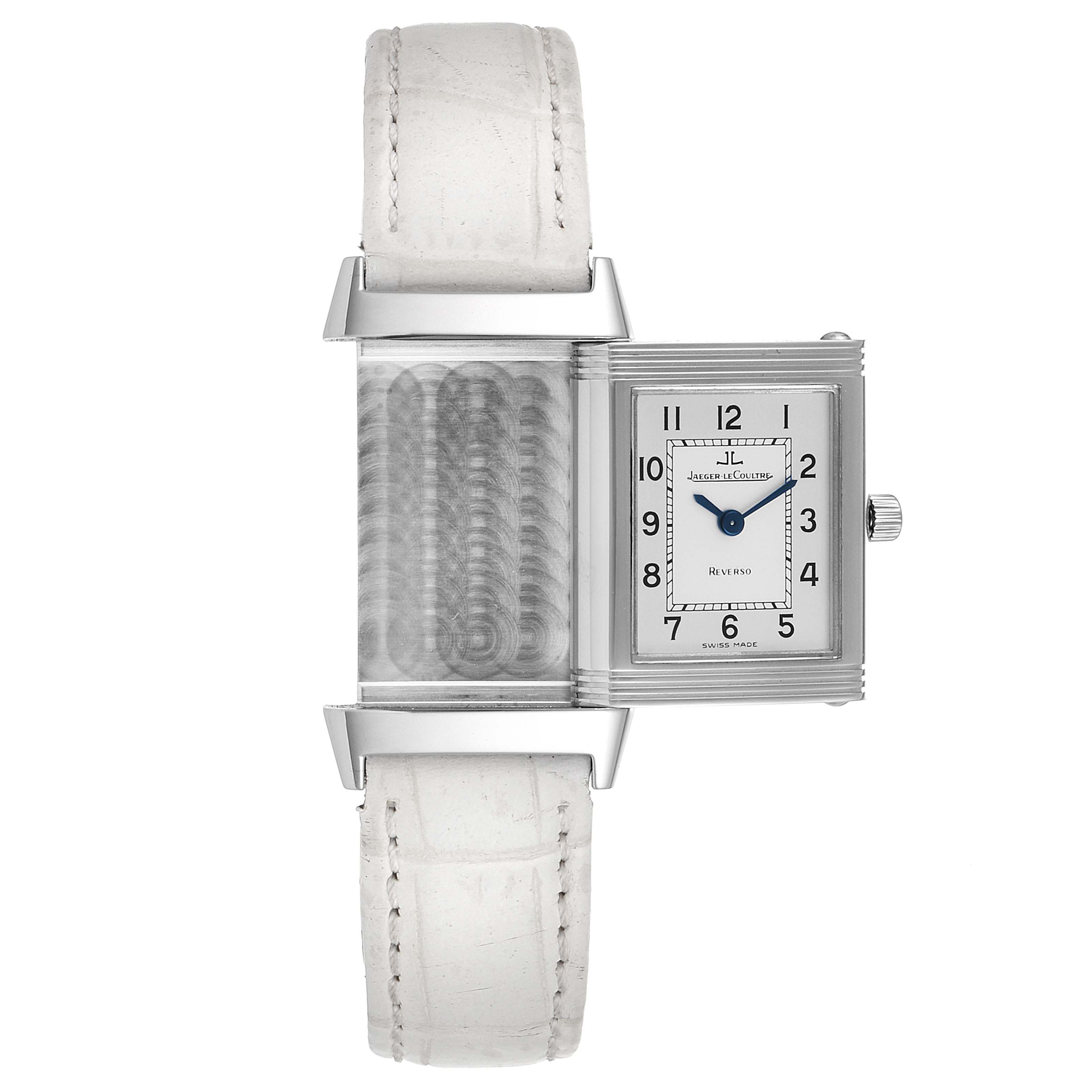 The image shows a Jaeger-LeCoultre Reverso watch with its reversible case mechanism halfway slid open, revealing the white leather strap and dial.