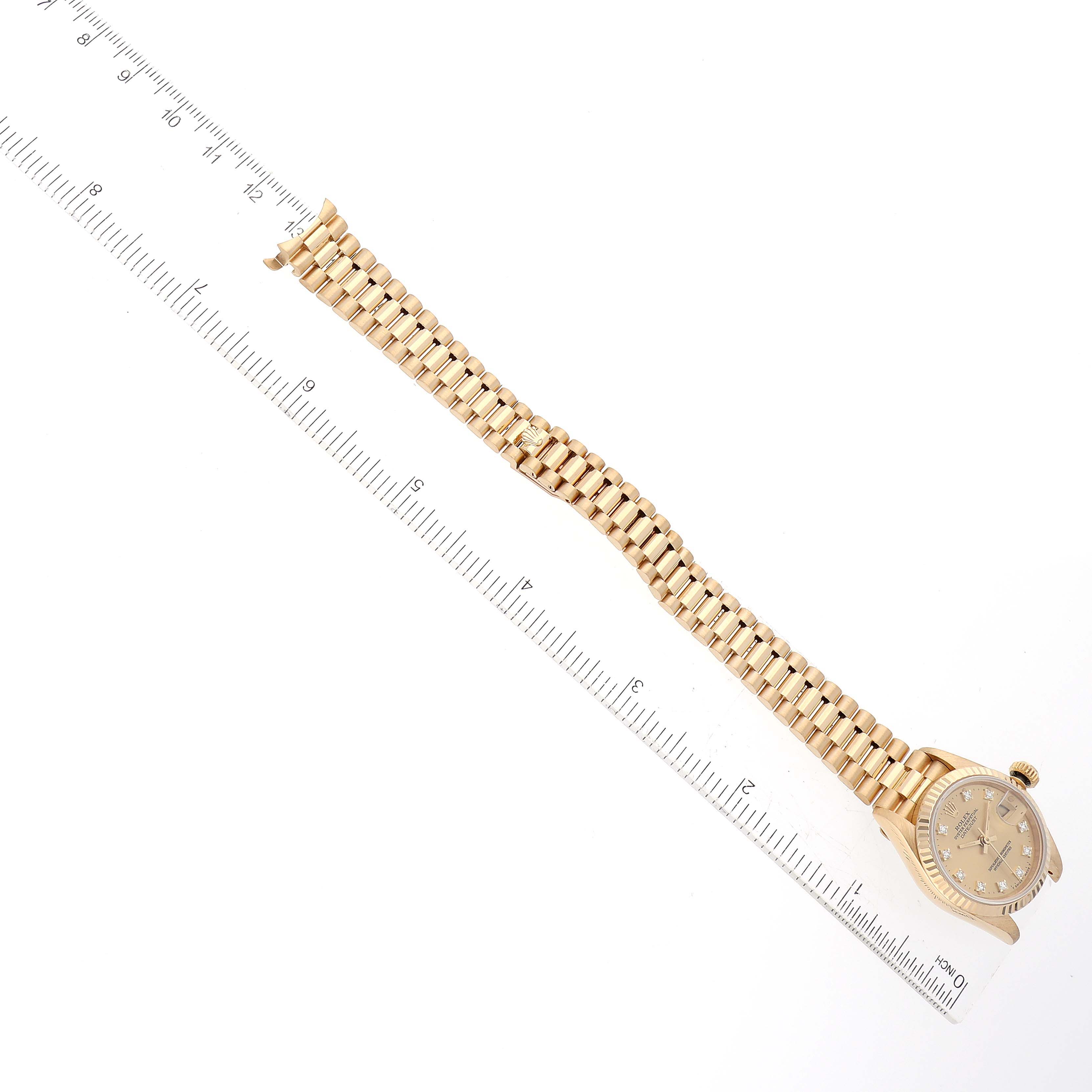 The image shows a Rolex President 69178 Women
s Yellow Gold Champagne Dial 69178 Women
s Yellow Gold Champagne Dial model watch laid flat, displaying its bracelet and dial, alongside a ruler for scale.