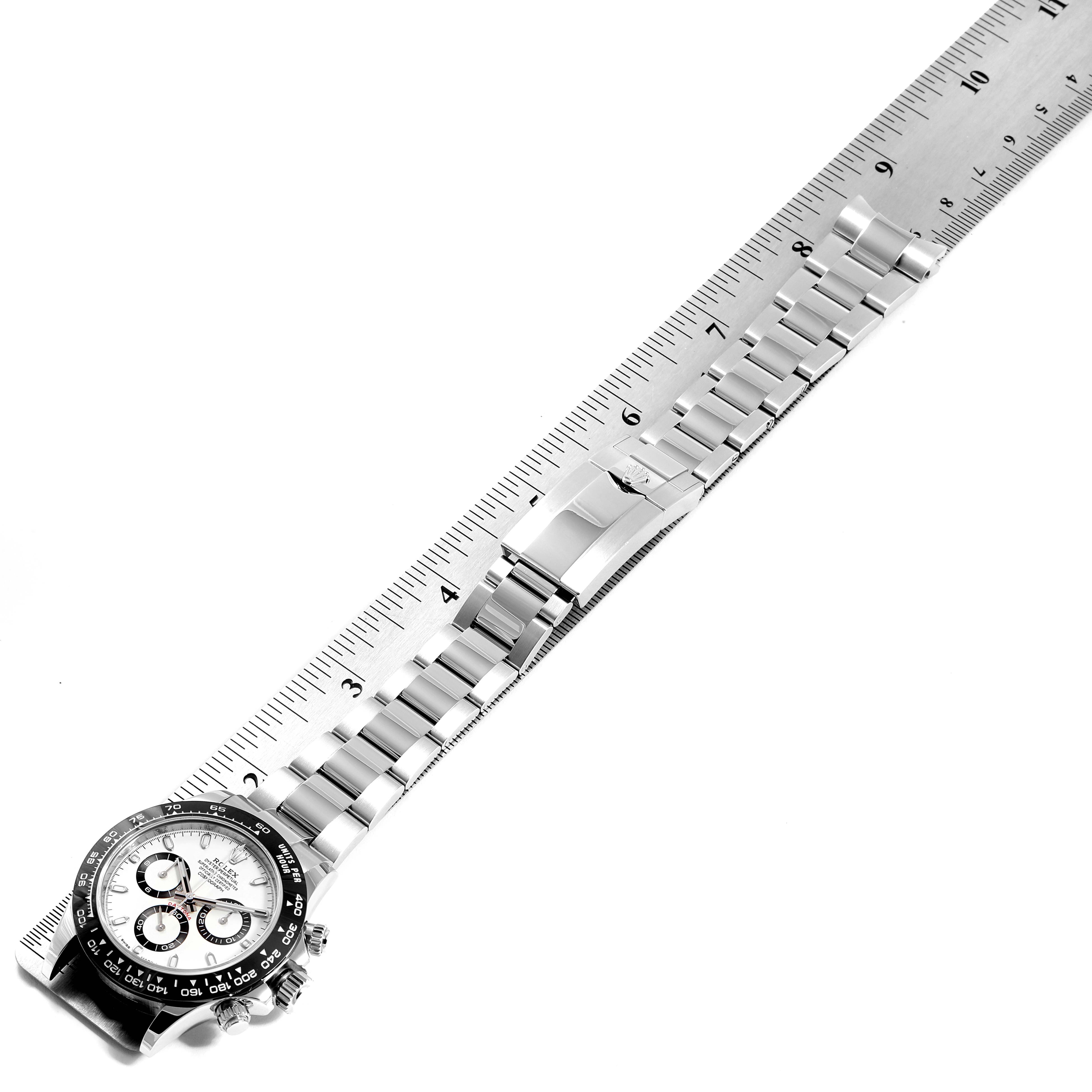 The image shows a top-down view of a Rolex Daytona 116500 Men's Stainless Steel White Dial 116500 Men's Stainless Steel White Dial watch, featuring its dial, bezel, and bracelet placed next to a ruler.