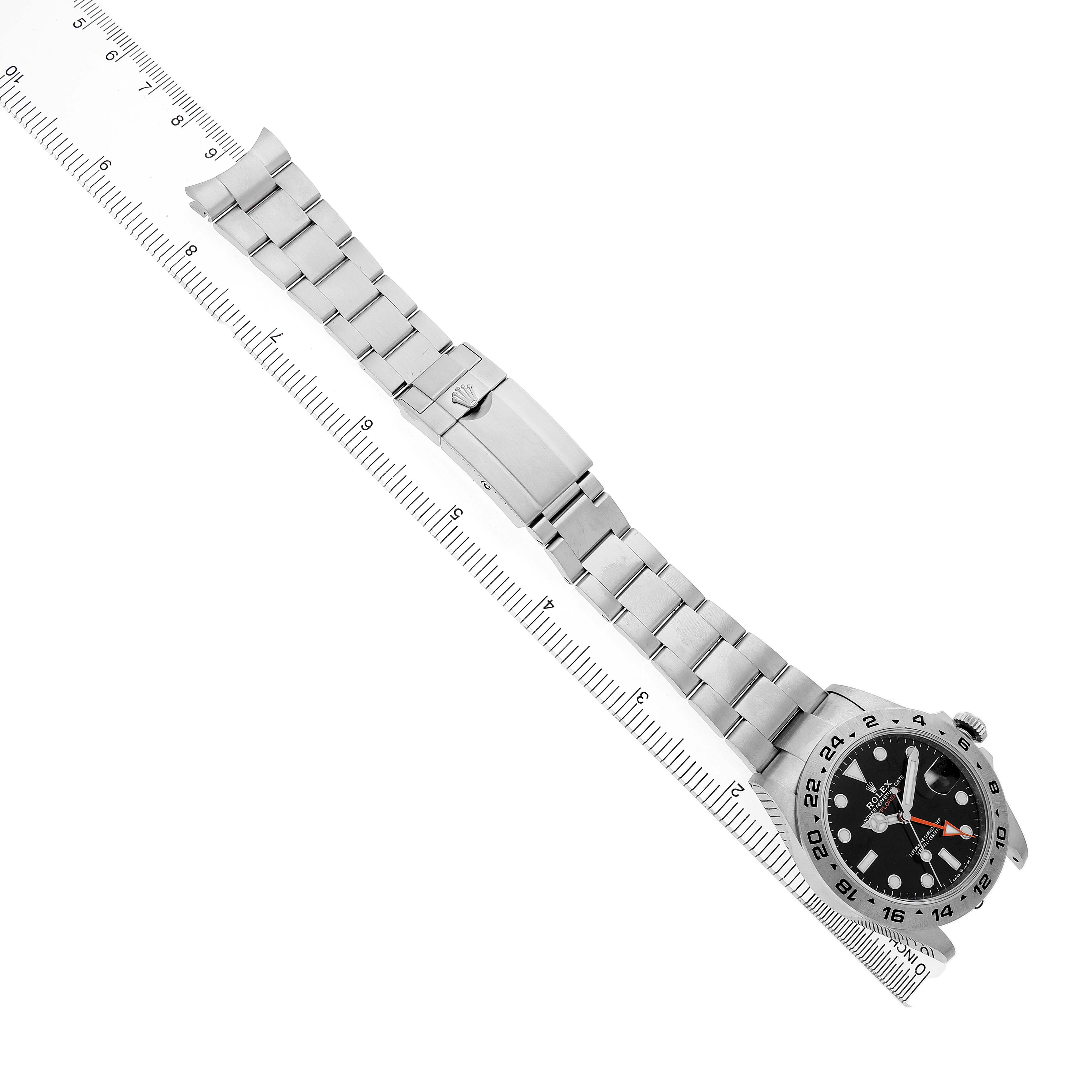 The image shows the Rolex Explorer 226570 Men's Stainless Steel Black Dial watch from an overhead angle, highlighting the face, bezel, and metal bracelet alongside a ruler.