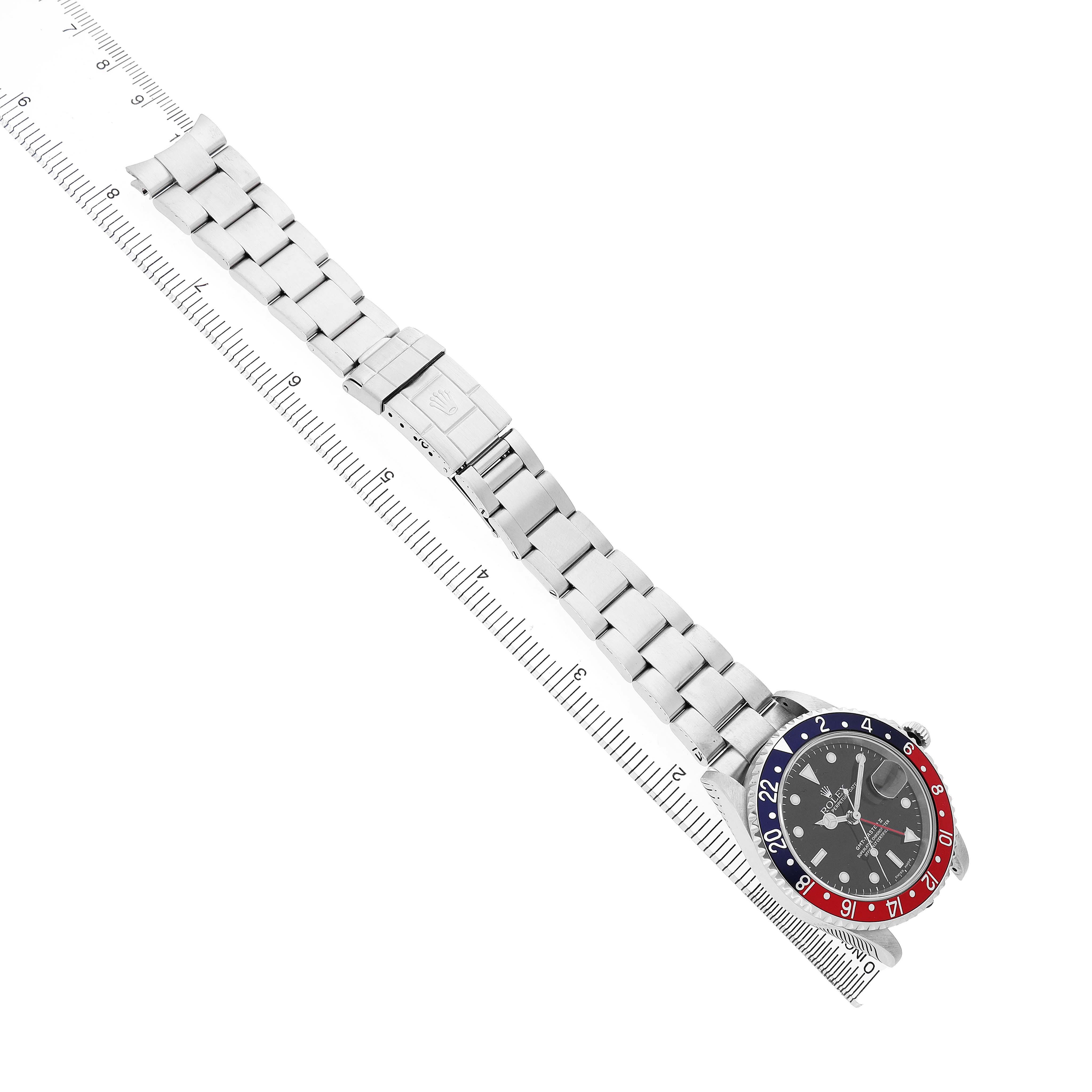 The image shows a top view of a Rolex GMT-Master 16710 Men's Stainless Steel Black Dial watch next to a ruler, displaying the entire bracelet and face.