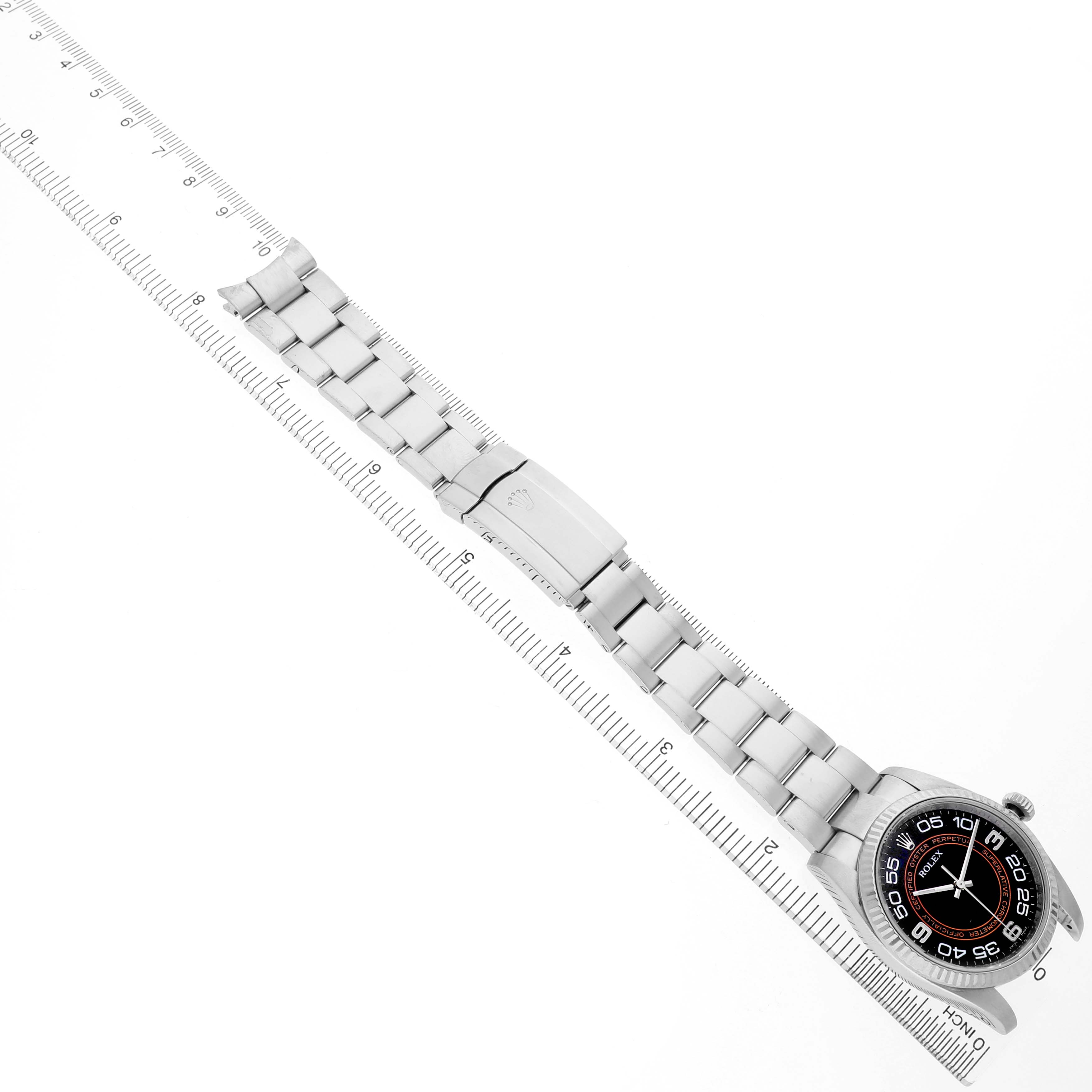 The Rolex Oyster Perpetual 116034 Men's Stainless Steel Black Dial watch is shown from an angled top view, displaying the dial and the full metal bracelet alongside a ruler.