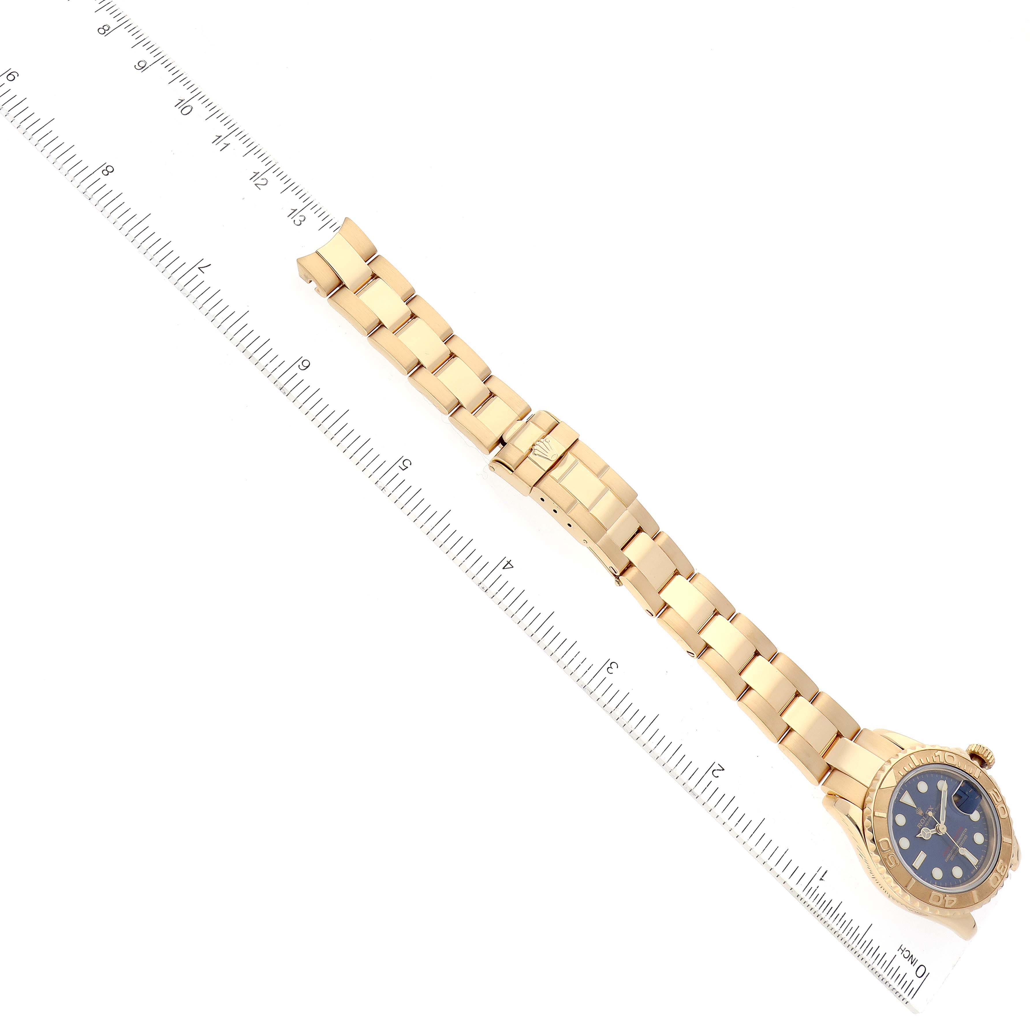 The image shows a top-down view of a Rolex Yacht-Master 69628 Women's Yellow Gold Blue Dial 69628 Women's Yellow Gold Blue Dial watch with a blue dial and gold bracelet next to a ruler.