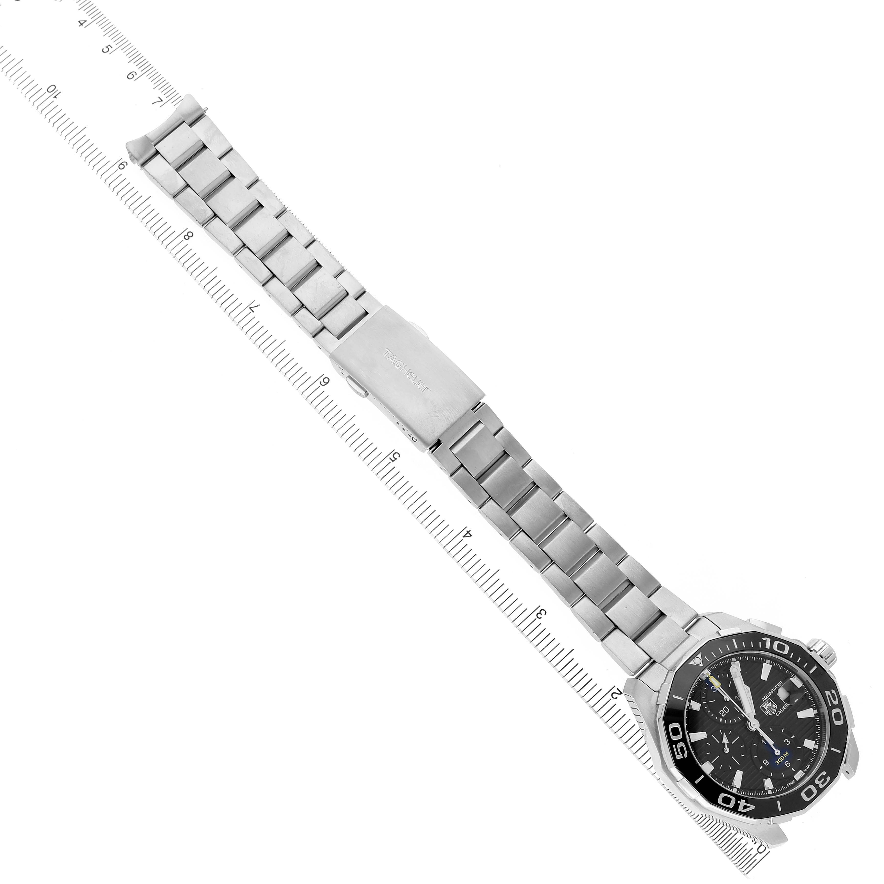 The Tag Heuer Aquaracer CAY211A.BA0927 Men's Stainless Steel Black Dial watch is shown from a top-down angle, displaying its face and full metal bracelet alongside a ruler.