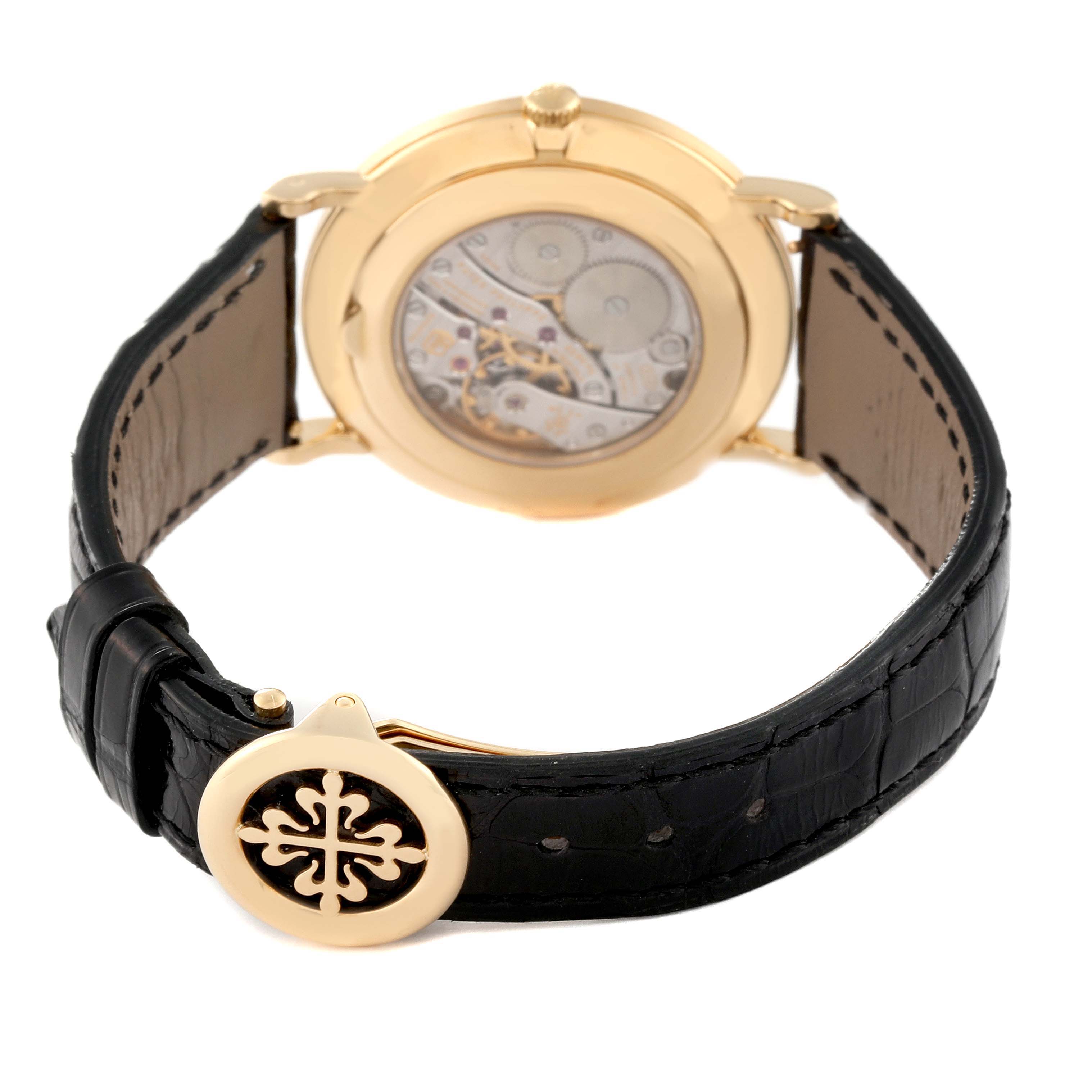 The image shows the back view of the Patek Philippe Calatrava 5119J Men's Yellow Gold White Dial 5119J Men's Yellow Gold White Dial watch, revealing its movement and a portion of the leather strap with the emblem.