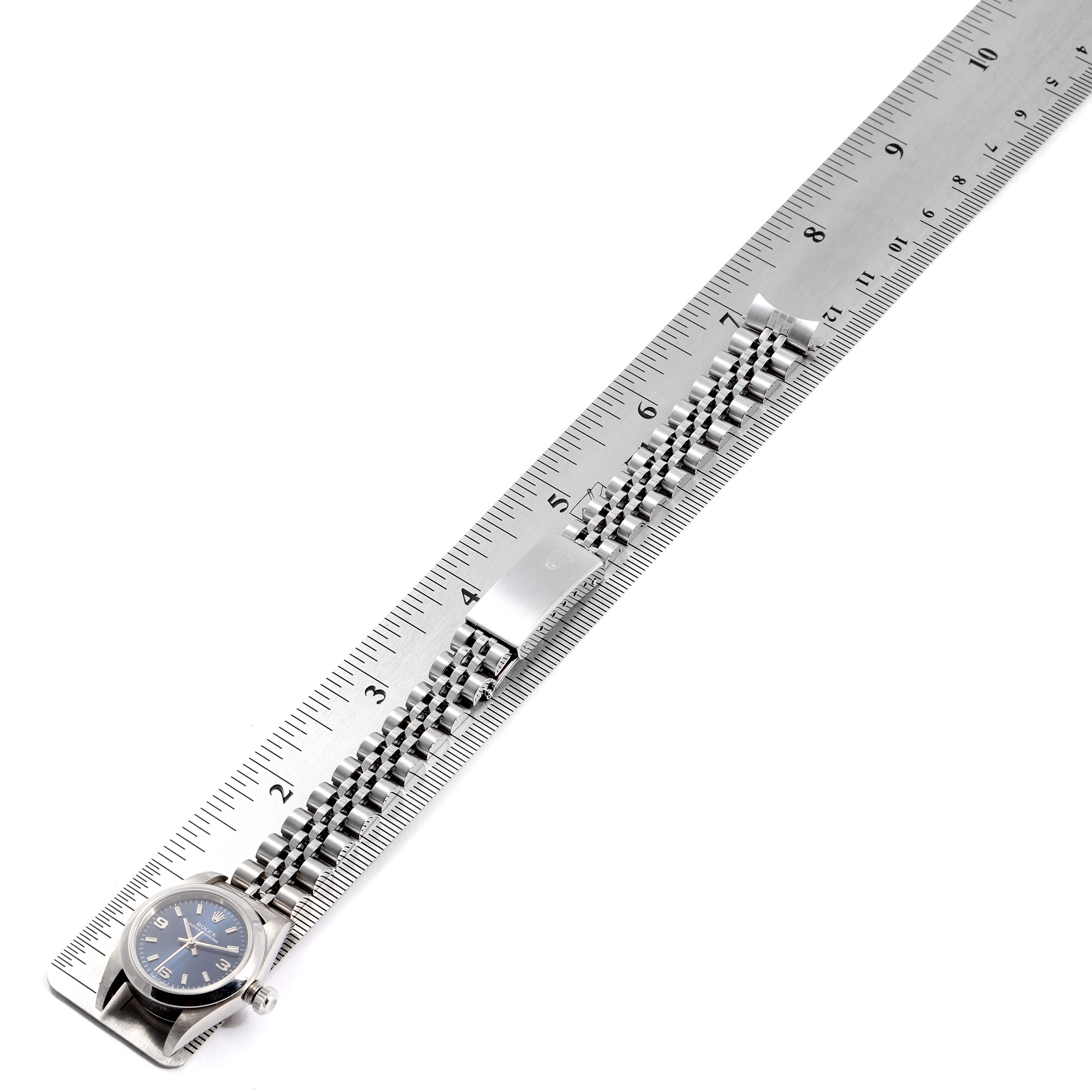 The image shows a top-down view of a Rolex Oyster Perpetual 76080 Women
s Stainless Steel Blue Dial 76080 Women
s Stainless Steel Blue Dial watch laid alongside a ruler, highlighting the watch face and metal band.