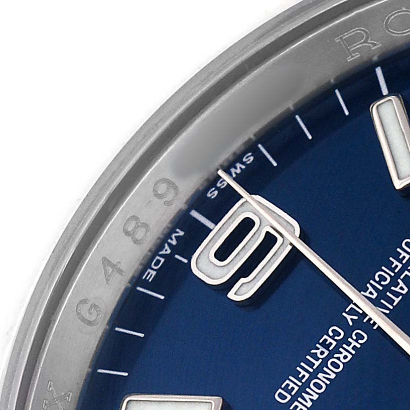 The image shows a close-up of the Rolex Oyster Perpetual 116000 Men's Stainless Steel Blue Dial watch dial, featuring hour markers, hands, and partial bezel engravings.