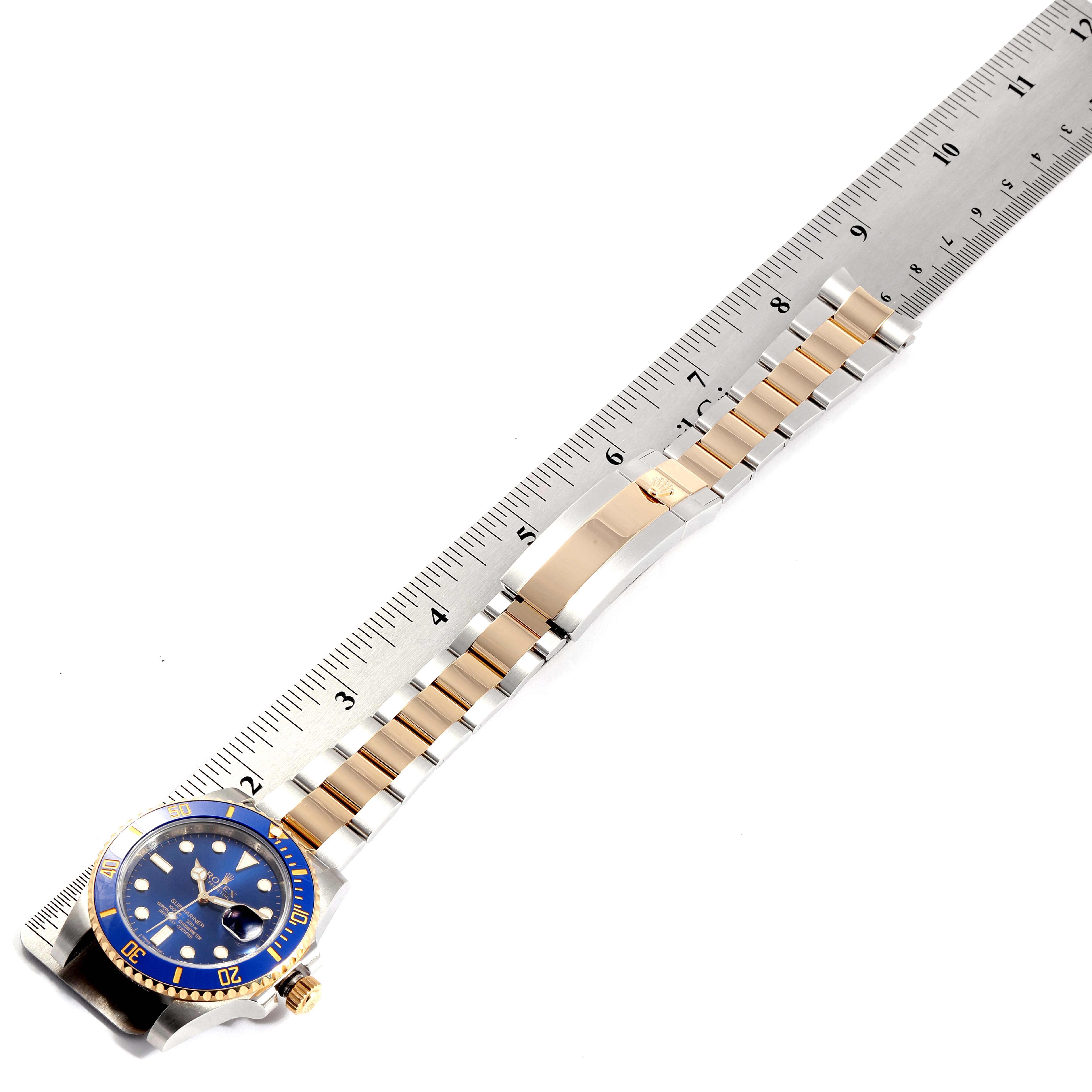 The image shows a Rolex Submariner 116613 Men's Stainless Steel Blue Dial 116613 Men's Stainless Steel Blue Dial watch placed alongside a ruler, highlighting its blue dial and gold and silver bracelet.