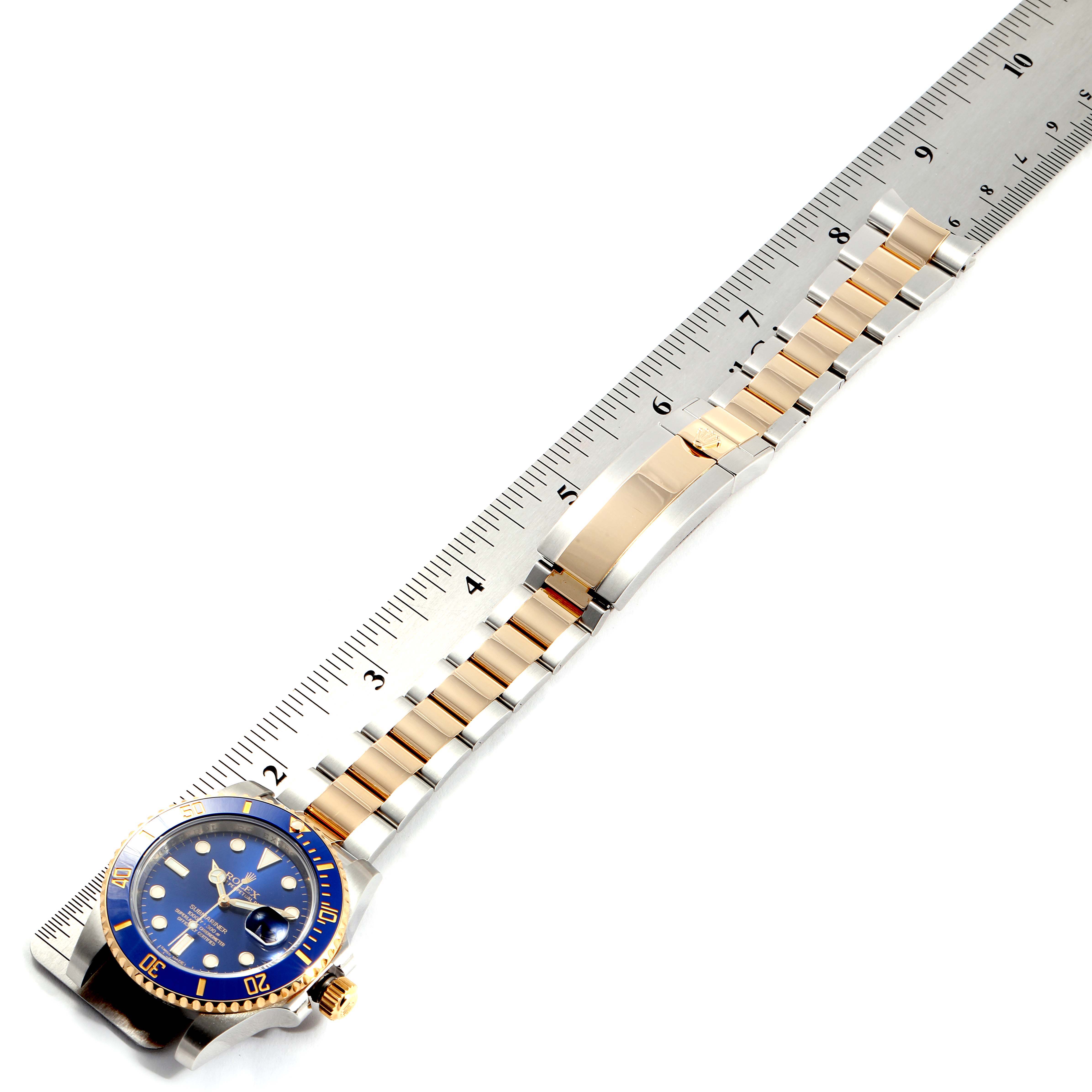 The image shows a Rolex Submariner 116613 Men
s Stainless Steel Blue Dial 116613 Men
s Stainless Steel Blue Dial watch at an angle displaying the face, crown, and band next to a ruler for scale.