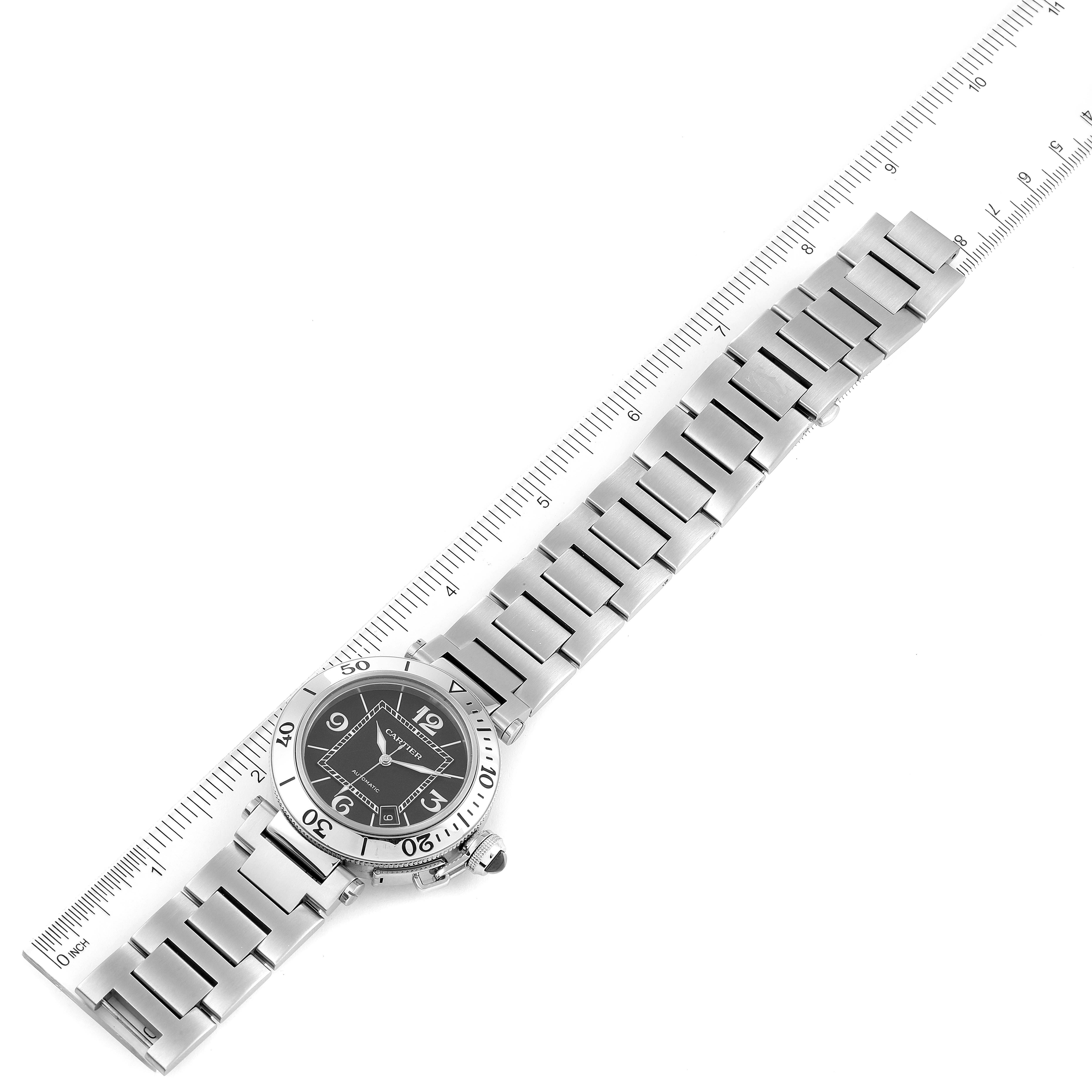 This image shows a top-down view of a Cartier Pasha W31077M7 Men
s Stainless Steel Black Dial W31077M7 Men
s Stainless Steel Black Dial watch displaying its entire face and bracelet alongside a ruler.