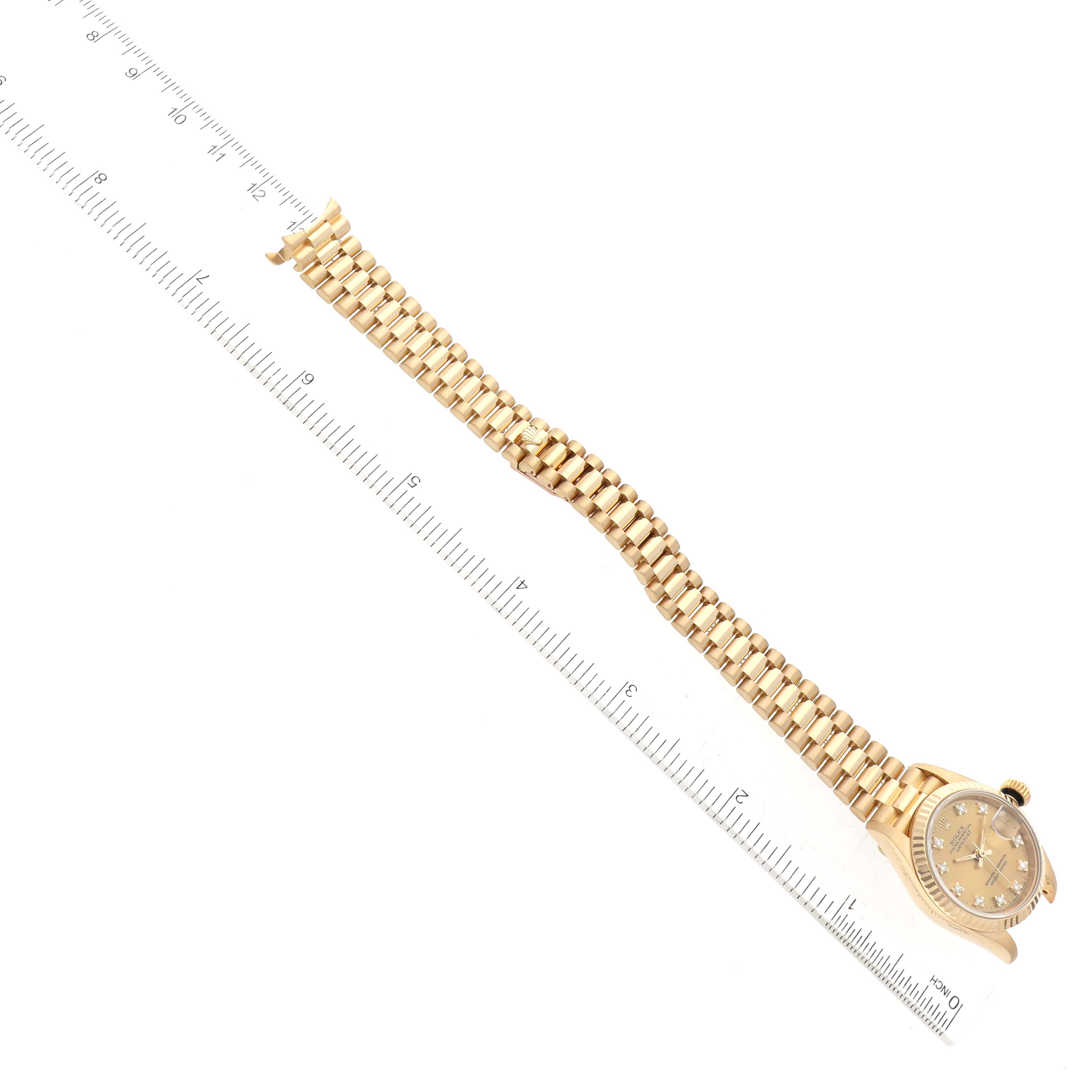 The image shows the Rolex President 69178 Women
s Yellow Gold Champagne Dial 69178 Women
s Yellow Gold Champagne Dial model watch from a top-down angle, displaying its face and full bracelet along with a ruler for size reference.