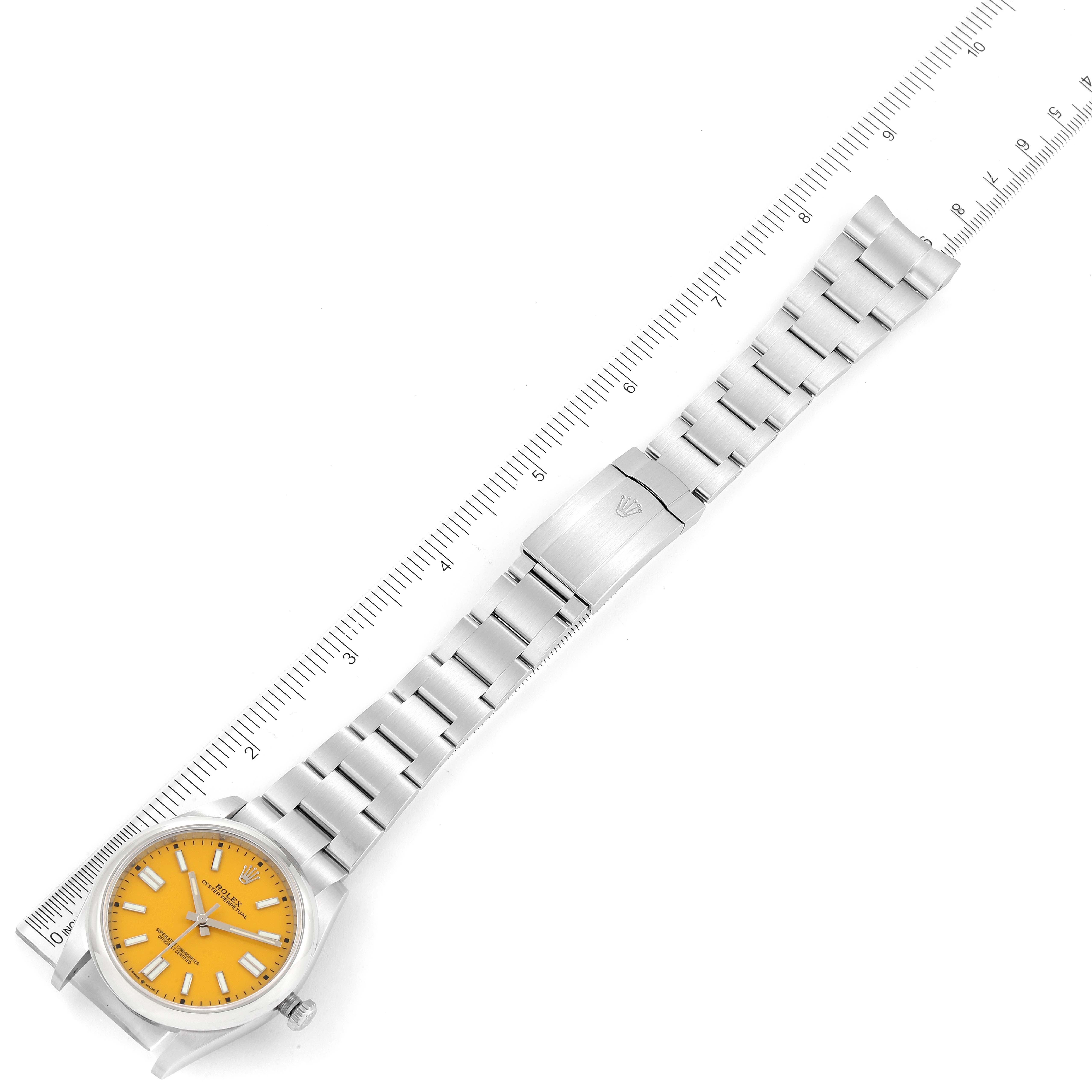 The Rolex Oyster Perpetual 124300 Men's Stainless Steel Yellow Dial 124300 Men's Stainless Steel Yellow Dial watch is shown in a top-down angle with its dial, bracelet, and clasp visible alongside a ruler.