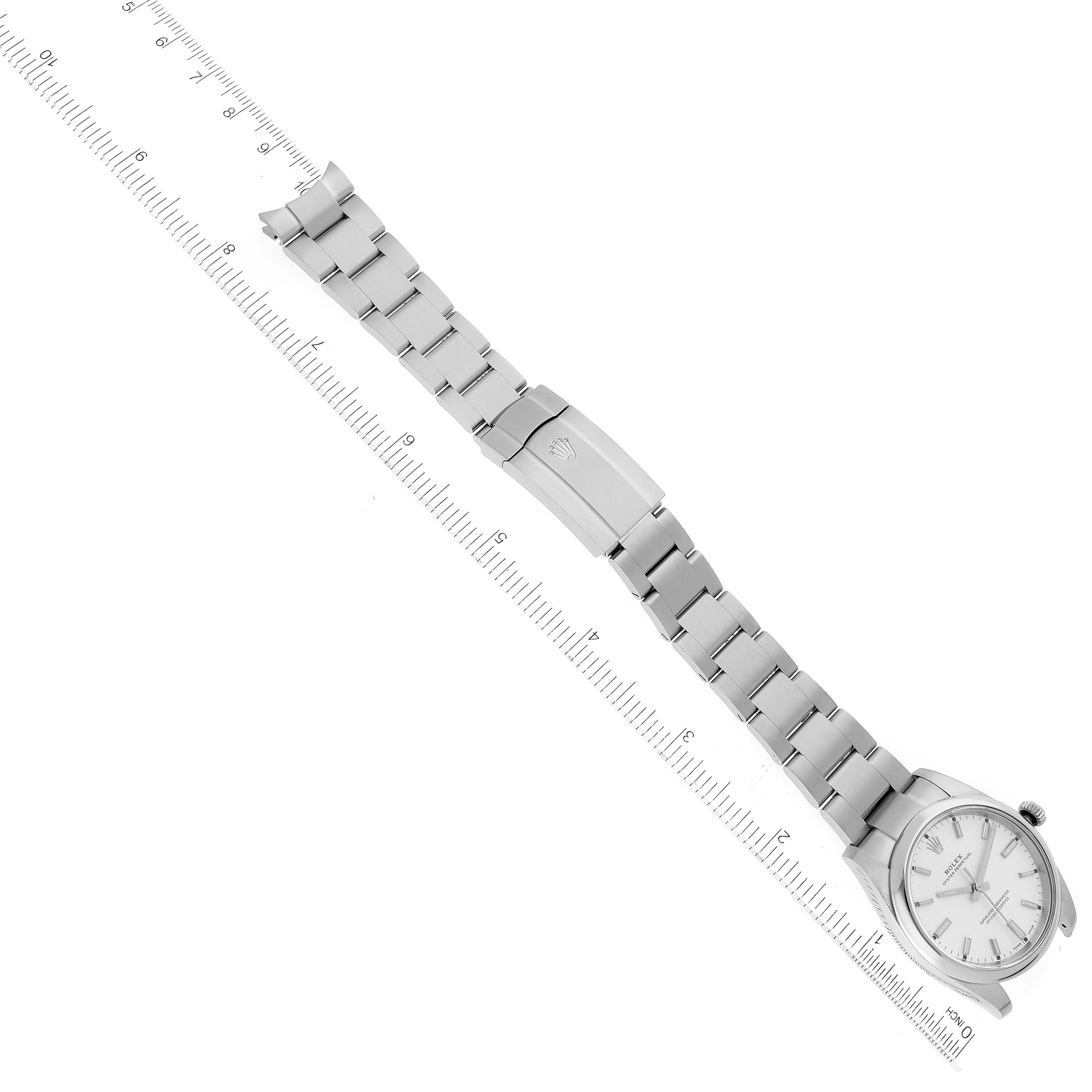 The Rolex Oyster Perpetual 114200 Men's Stainless Steel Silver Dial watch is shown in a flat, top-down angle with the bracelet and clasp extended alongside a ruler.