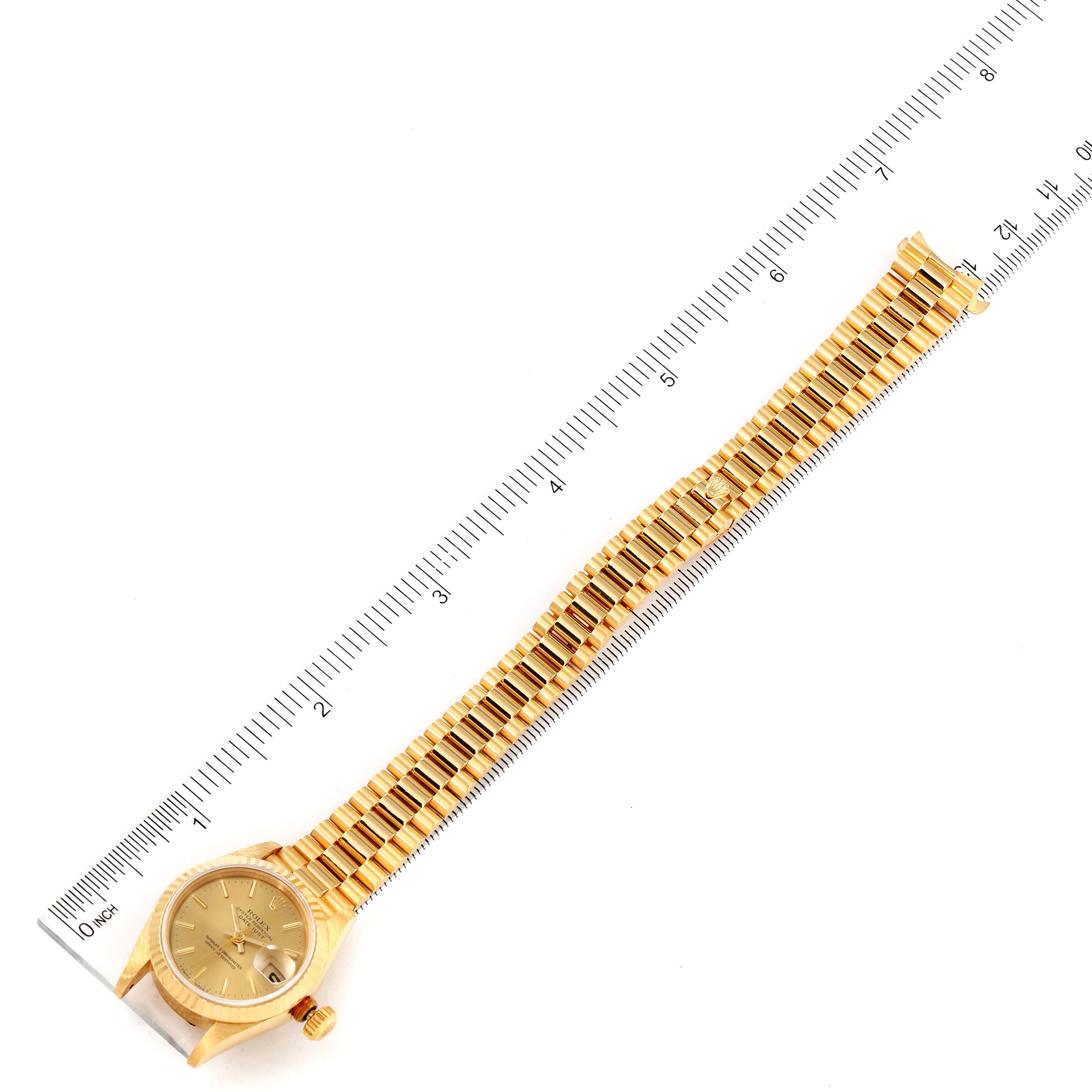 The image shows an overhead view of a Rolex President 69178 Women
s Yellow Gold Champagne Dial 69178 Women
s Yellow Gold Champagne Dial model watch, including the dial, crown, and bracelet, along with a ruler for scale.