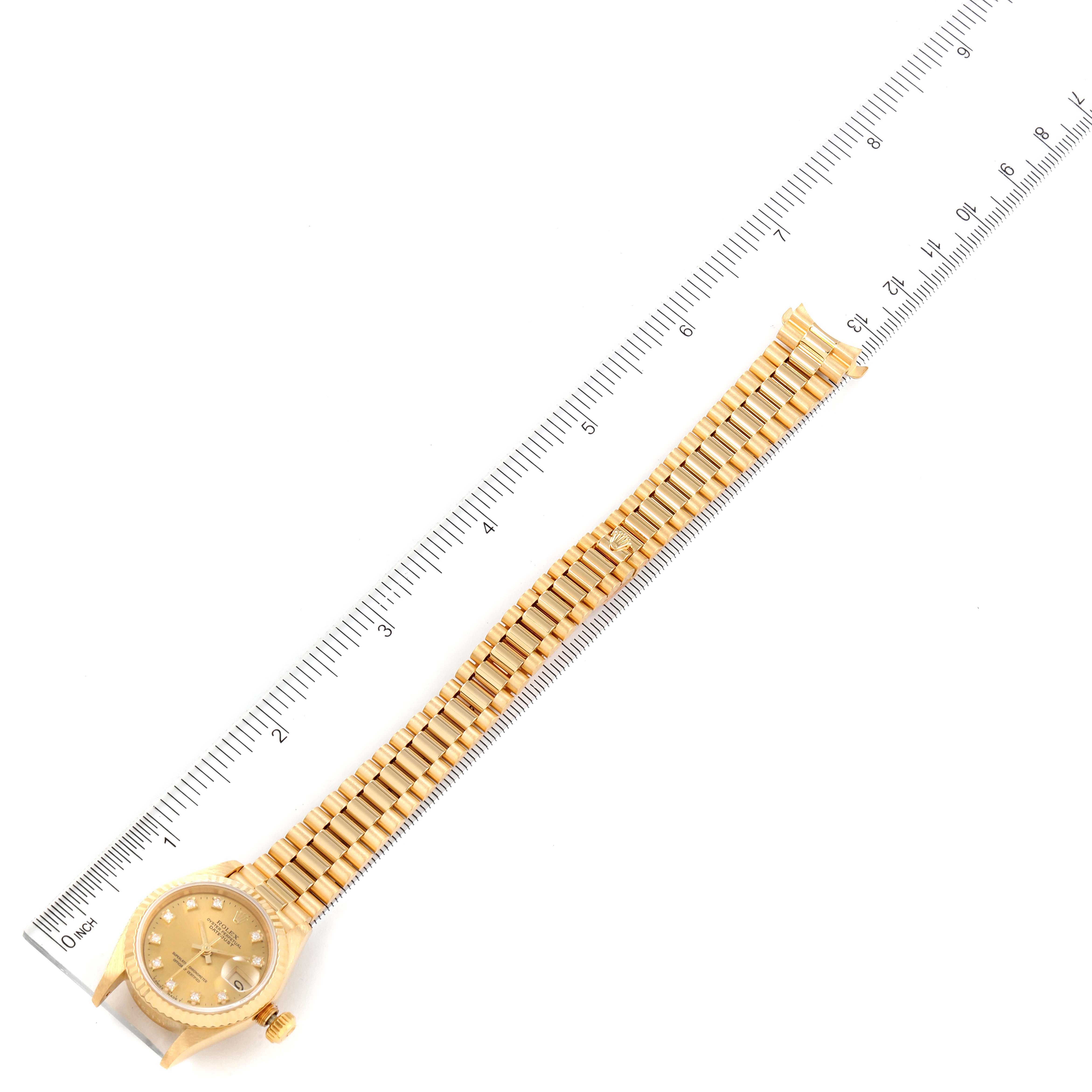 The image shows a Rolex President 69178 Women
s Yellow Gold Champagne Dial 69178 Women
s Yellow Gold Champagne Dial model watch, fully extended with the face and bracelet laid next to a ruler for scale.