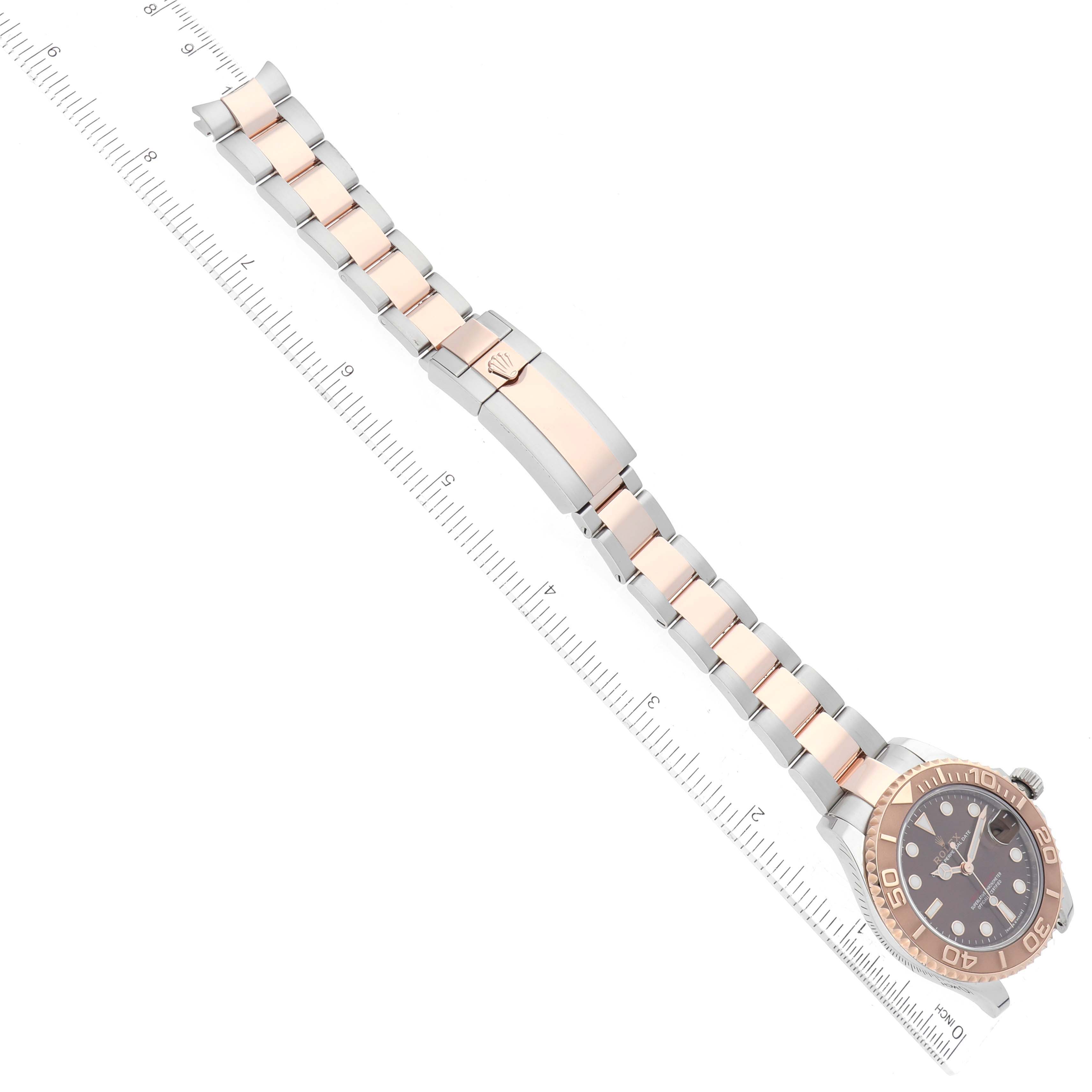 The image shows a top view of the Rolex Yacht-Master 268621 Men's Steel and Gold (two tone) Brown Dial 268621 Men's Steel and Gold (two tone) Brown Dial watch, highlighting the complete band and face with a measuring scale nearby.