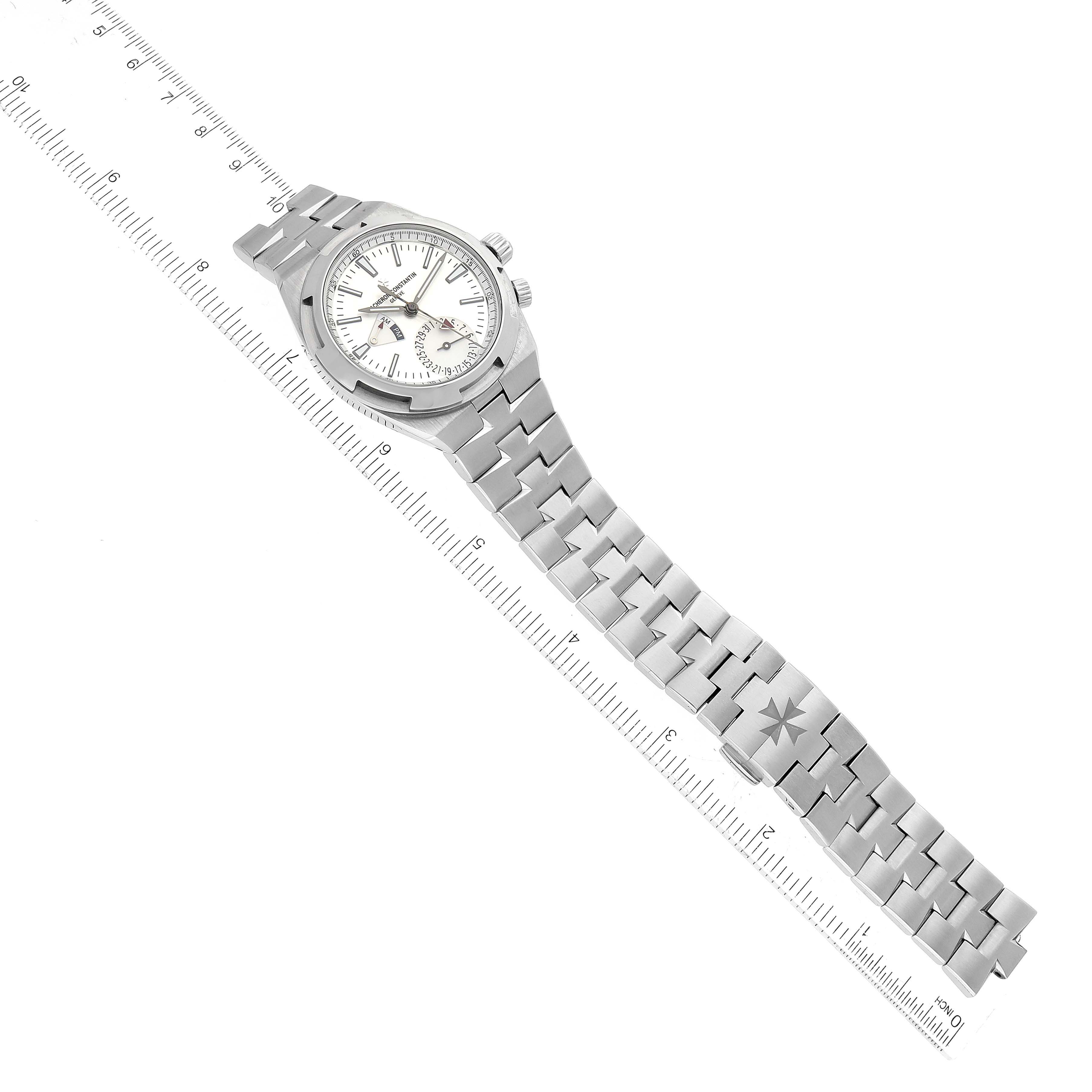The image shows a Vacheron Constantin Overseas 7900V/110A Men's Stainless Steel Silver Dial 7900V/110A Men's Stainless Steel Silver Dial watch laid flat on a ruler, displaying the entire watch from the bracelet to the face.