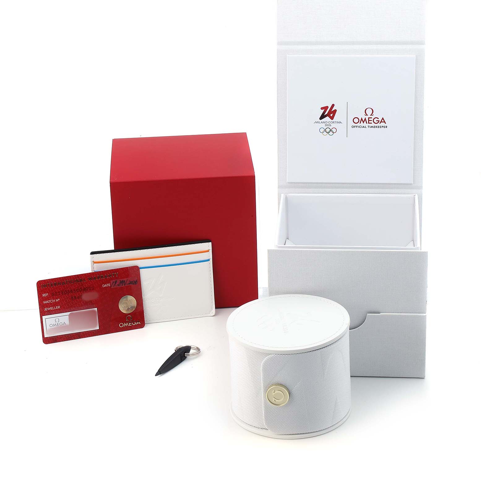 The image shows the Omega Speedmaster 324.30.38.40.04.001 Men's Stainless Steel White Dial box, warranty cards, a cylindrical case, and a key-like accessory.