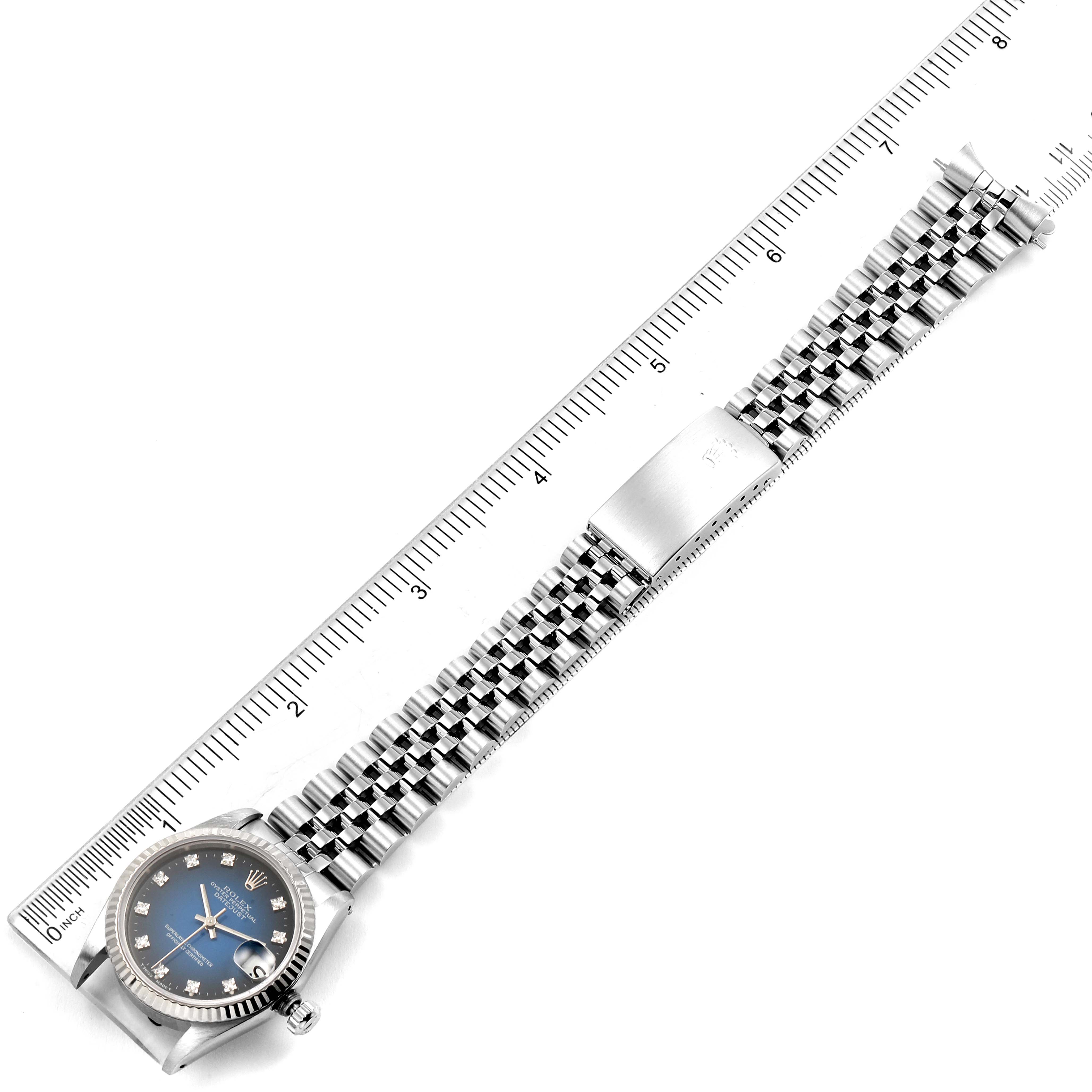 The image shows a top view of a Rolex Mid-Size 68274 Women's Stainless Steel Blue Dial 68274 Women's Stainless Steel Blue Dial watch with its full stainless steel bracelet laid out next to a ruler.