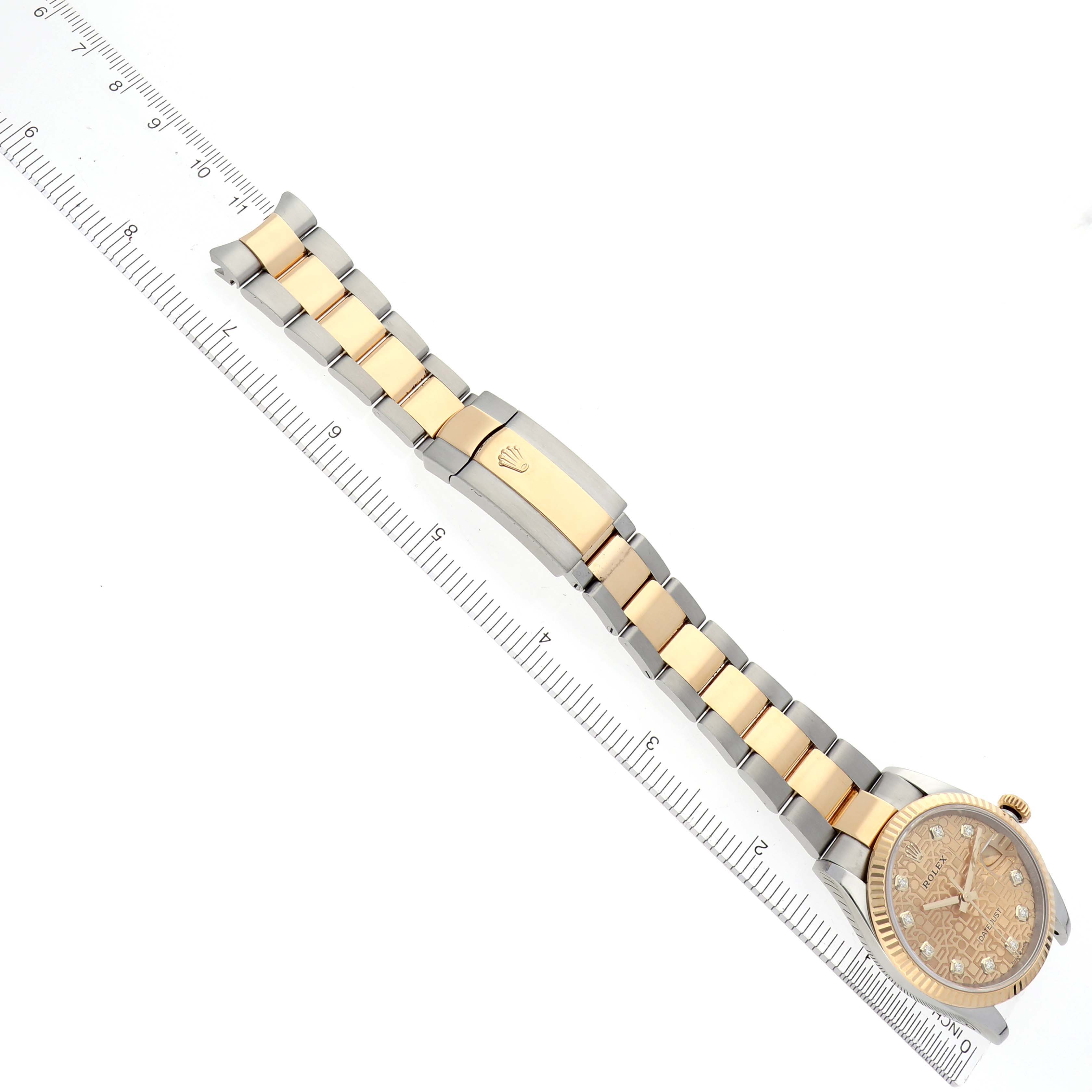 The Rolex Datejust 126233 Men's Steel and Gold (two tone) Champagne Dial 126233 Men's Steel and Gold (two tone) Champagne Dial watch is shown at a diagonal angle focusing on the band and clasp alongside a ruler.