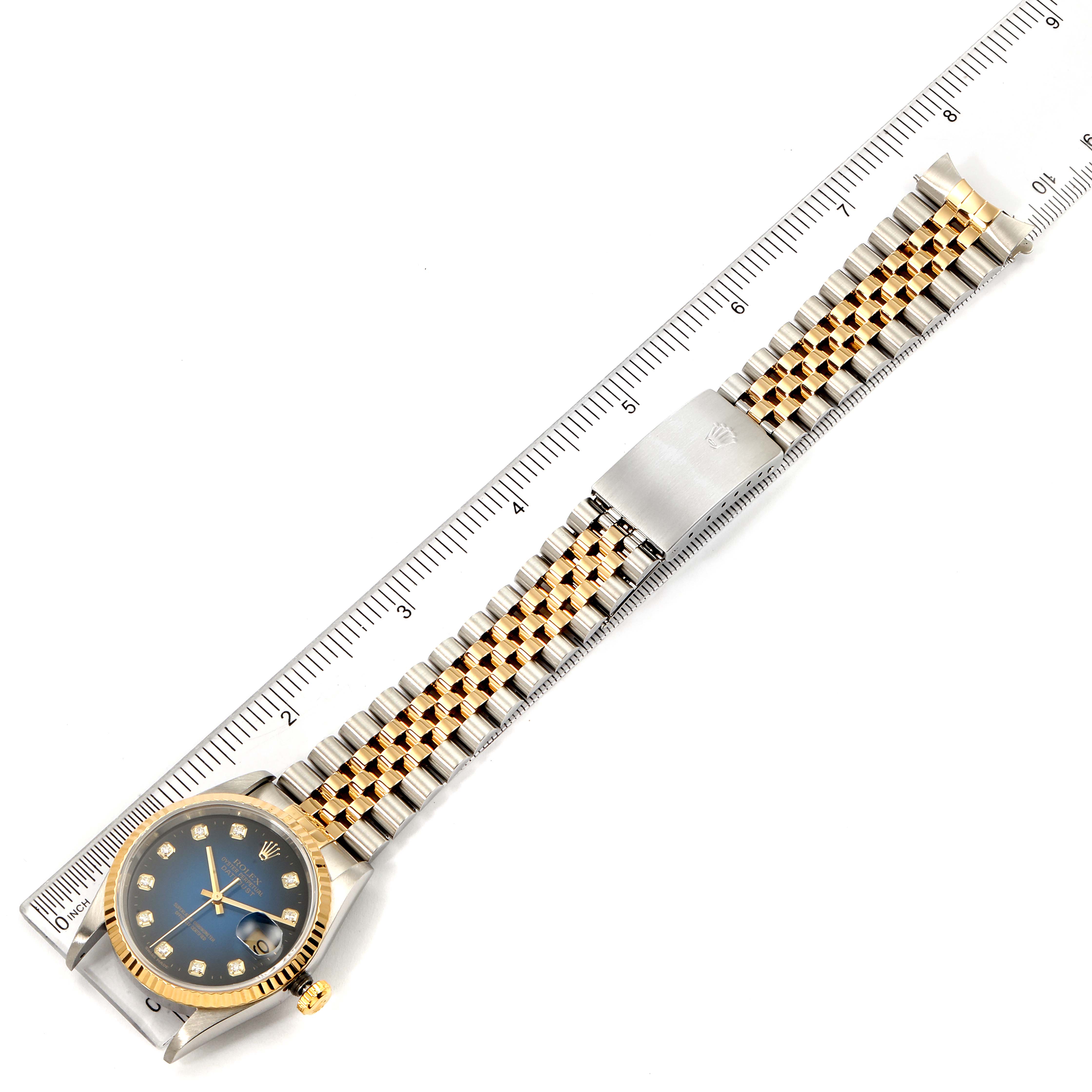 The image shows a top-down view of a Rolex Datejust 16233 Men's Steel and Gold (two tone) Blue Dial 16233 Men's Steel and Gold (two tone) Blue Dial watch, including the face, bezel, and bracelet alongside a ruler for scale.