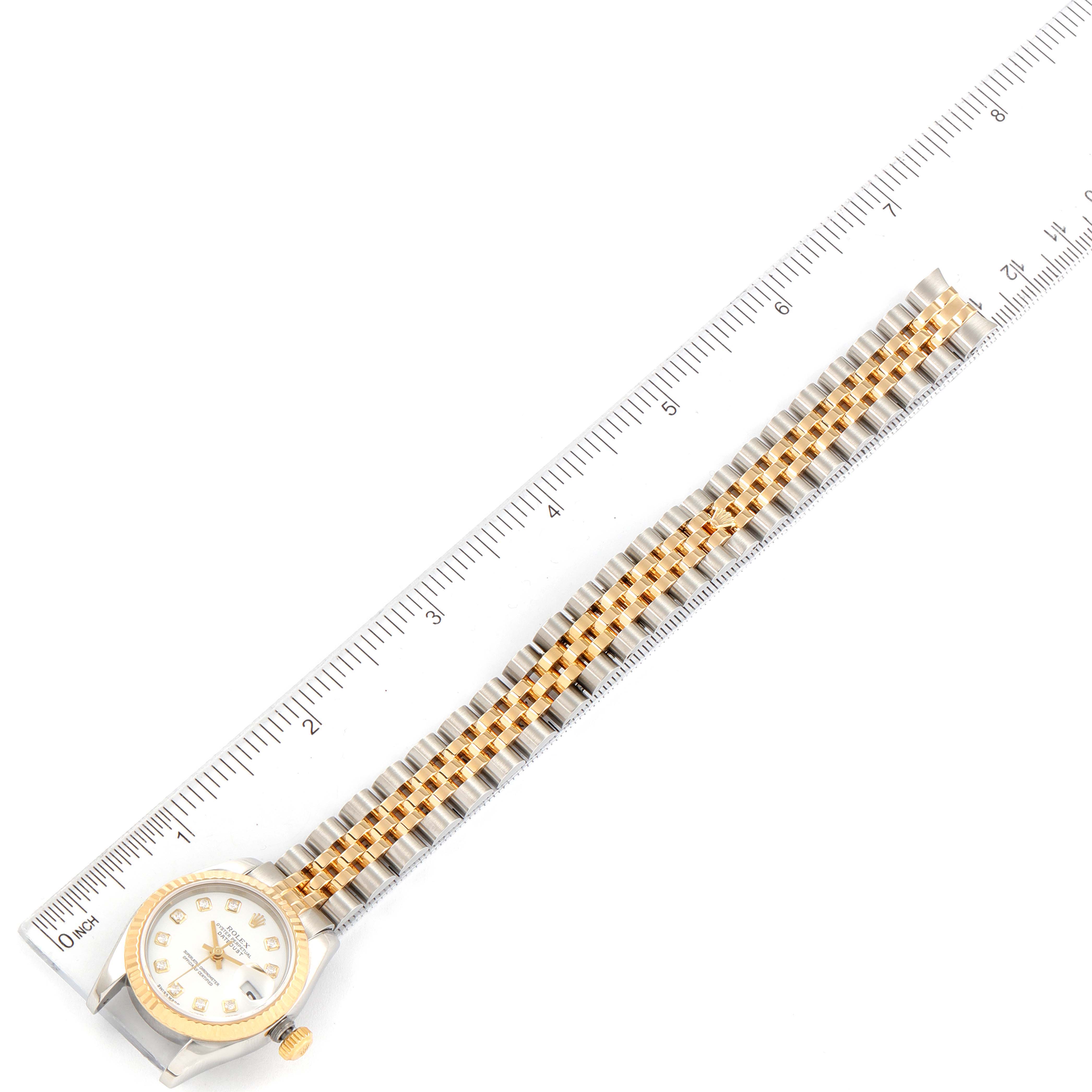 The image shows a top-down view of a Rolex Datejust 179173 Women's Steel and Gold (two tone) White Dial 179173 Women's Steel and Gold (two tone) White Dial watch alongside a ruler.
