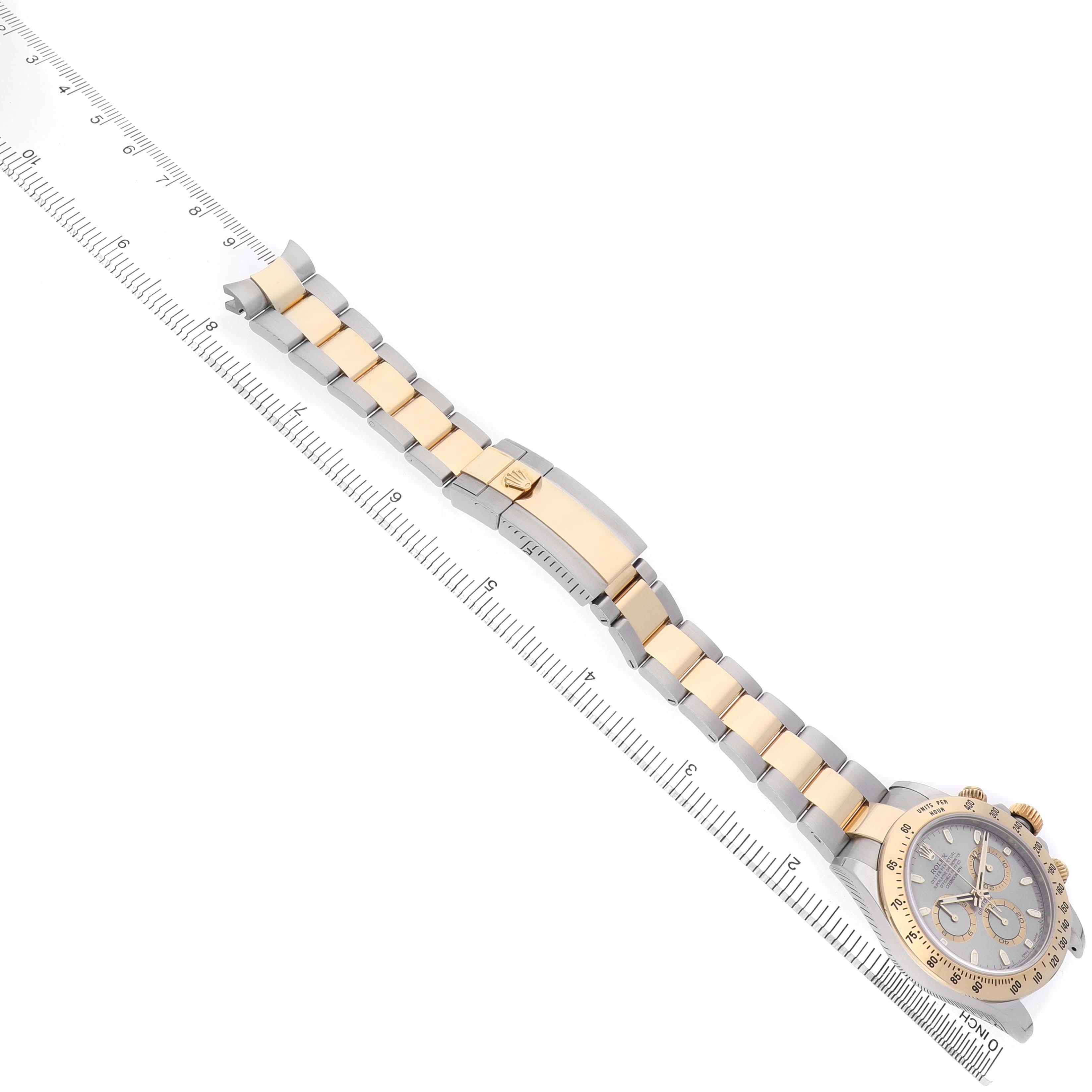 The Rolex Daytona 116523 Men's Steel and Gold (two tone) Silver Dial watch is shown laid flat at an angle, displaying the bracelet and clasp alongside a ruler for scale.