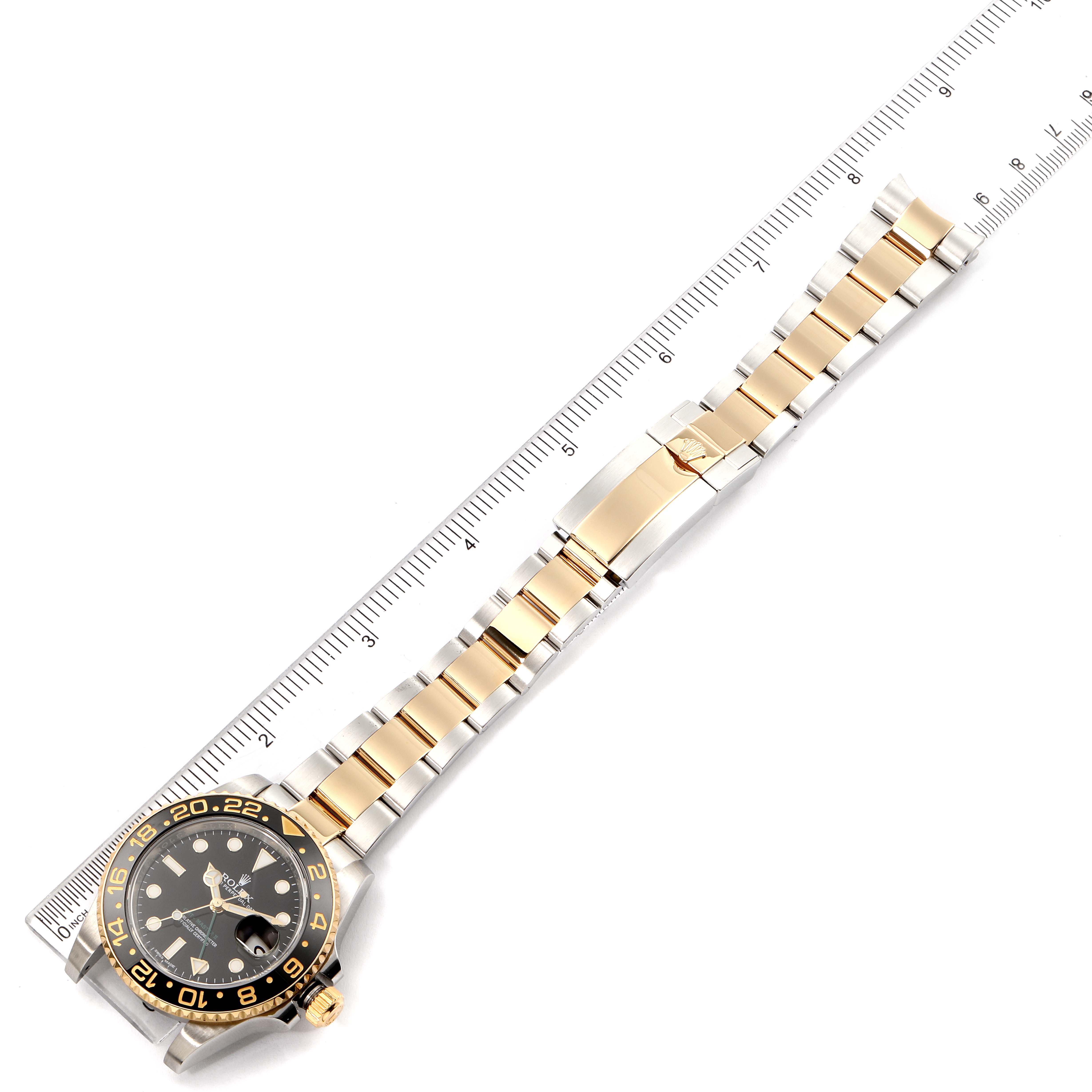 The image shows a top view of a Rolex GMT-Master 116713 Men
s Steel and Gold (two tone) Black Dial 116713 Men
s Steel and Gold (two tone) Black Dial watch and its two-tone bracelet, next to a measuring ruler.