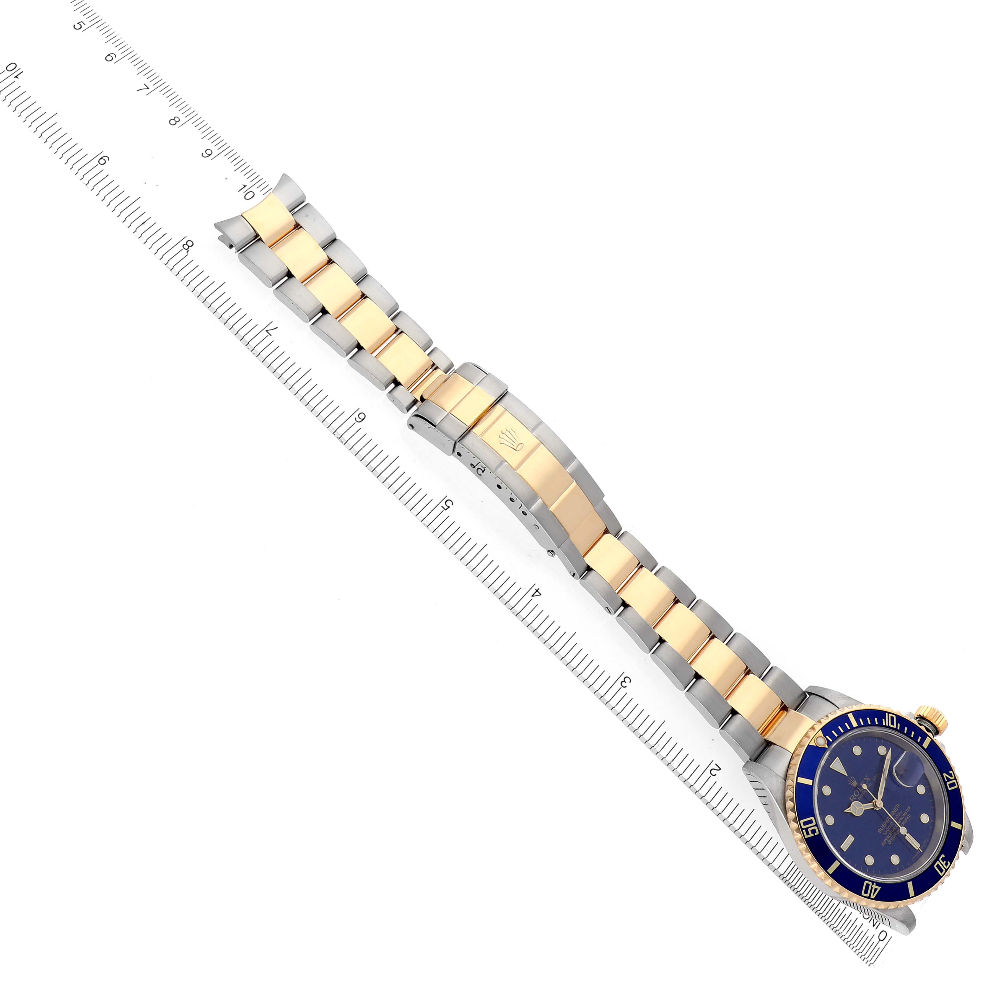 The Rolex Submariner 16613 Men's Steel and Gold (two tone) Blue Dial 16613 Men's Steel and Gold (two tone) Blue Dial watch is shown at a top view, highlighting the blue dial, bezel, and gold and silver bracelet against a ruler.