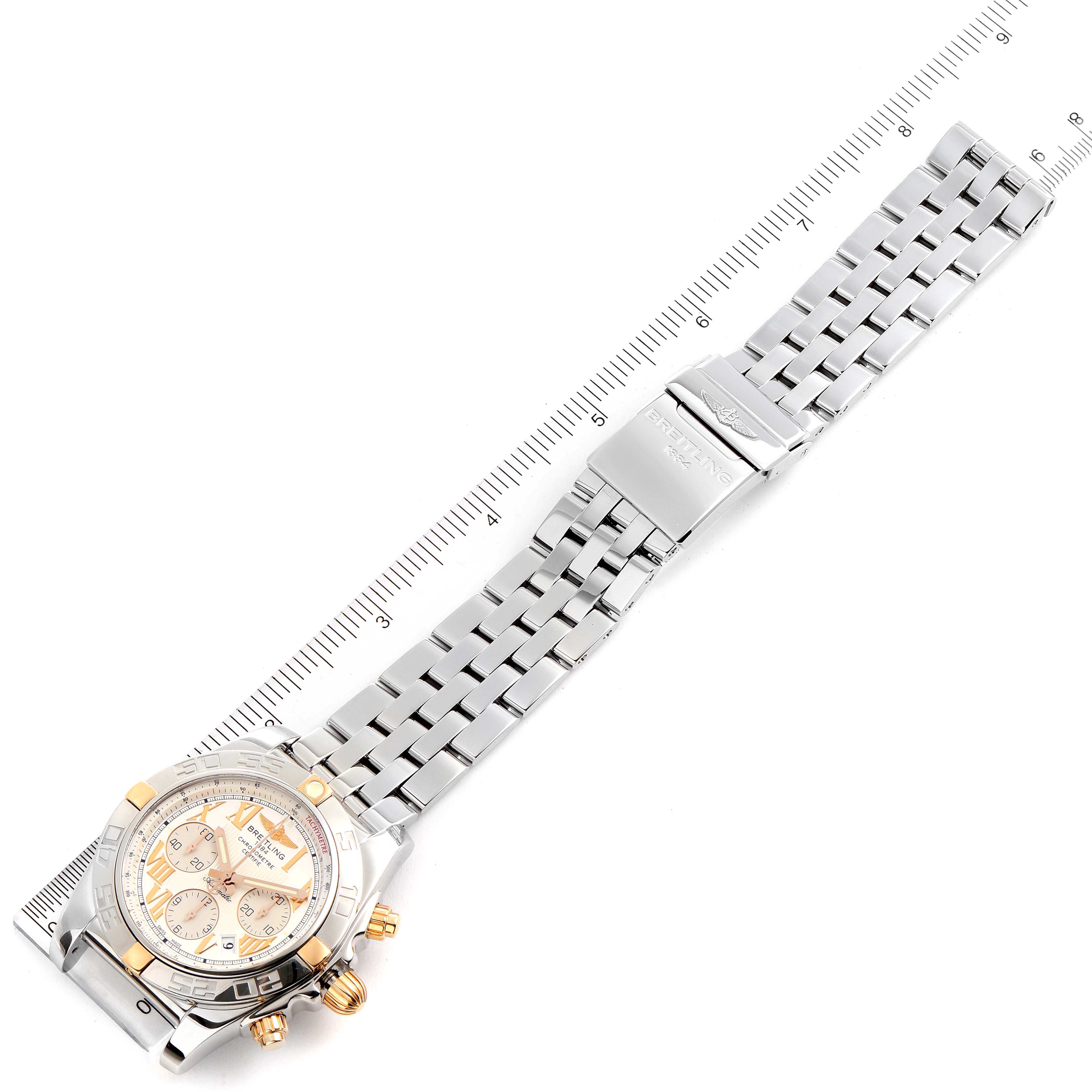 The image shows a Breitling Chronomat IB0110 Men
s Stainless Steel Silver Dial IB0110 Men
s Stainless Steel Silver Dial watch laid flat with the full bracelet and the dial visible, alongside a measuring scale.