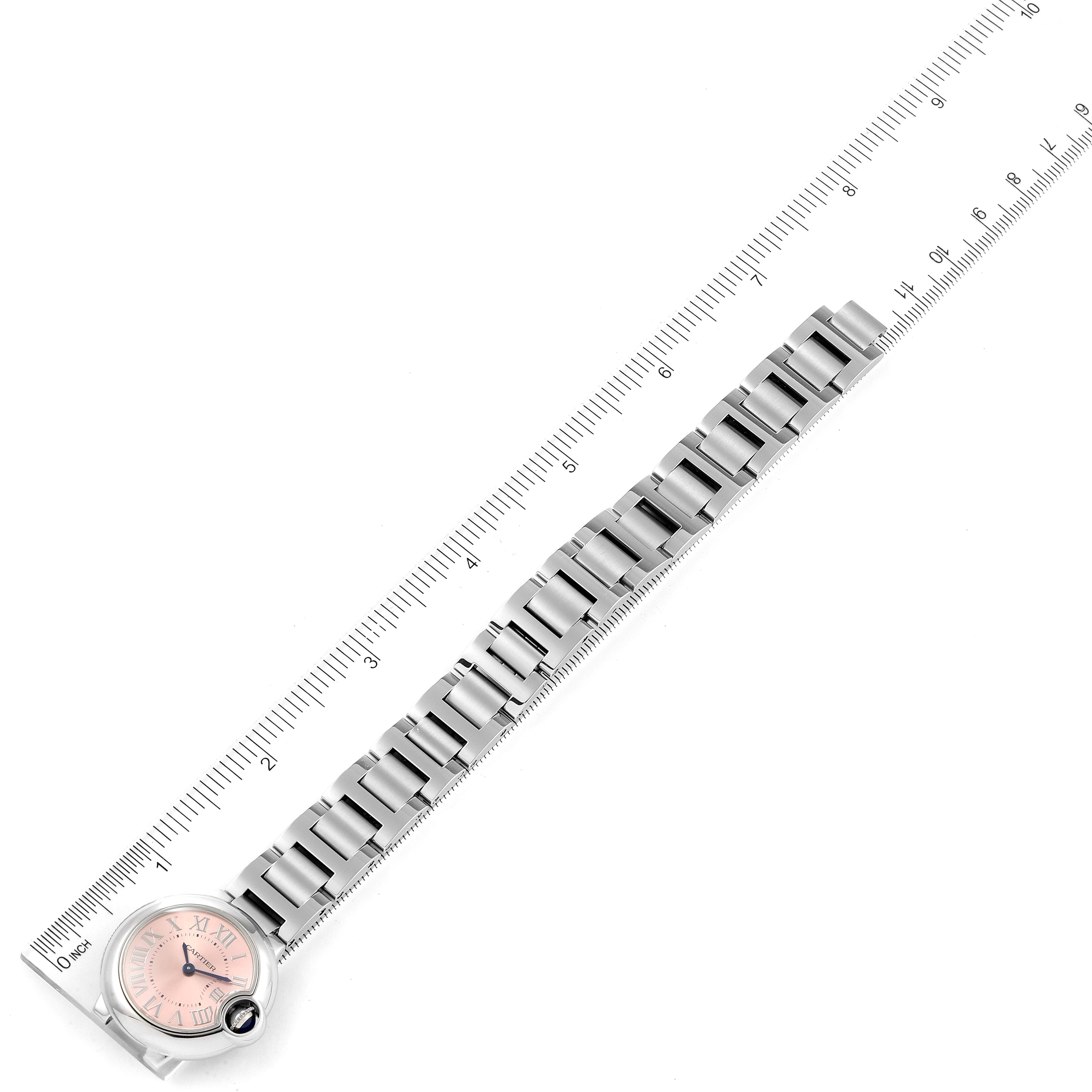 The image shows a Ballon Bleu model by Cartier, featuring its face and full metal bracelet, laid alongside a measuring ruler.